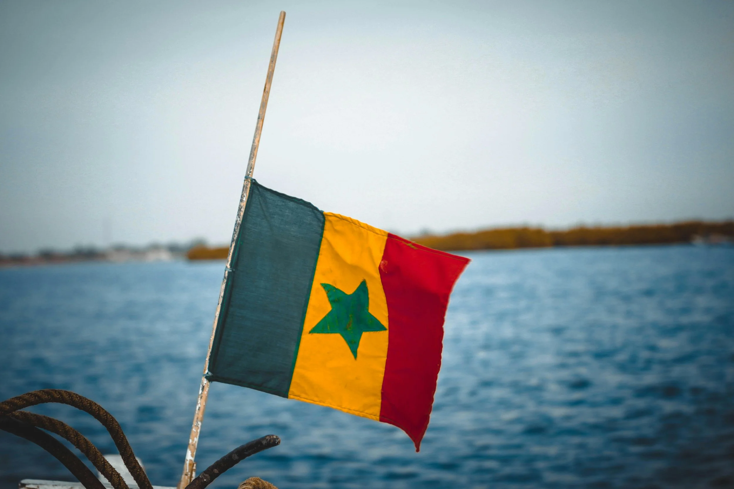 Drapeau du Sénégal flottant sur l'eau à bord d'un bateau avec un horizon fluvial en arrière-plan.
