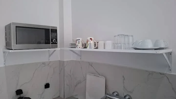 Étagère murale avec un micro-ondes, des mugs, des verres, et des tasses dans une cuisine moderne.