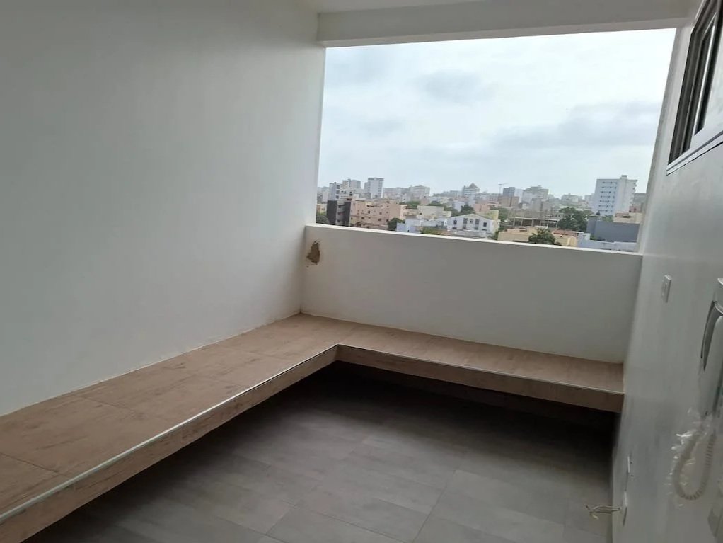 Balcon vide avec vue sur une ville urbaine, murs blancs, sol en bois foncé.