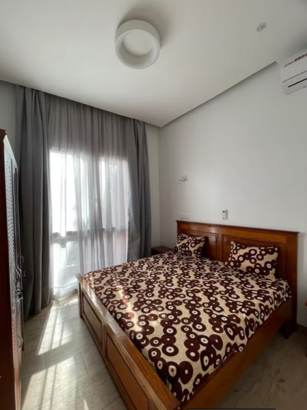 Chambre avec lit en bois, literie à motifs circulars marron, rideaux gris, fenêtre donnant sur l'extérieur, climatisation murale, plafond avec luminaire, mur blanc