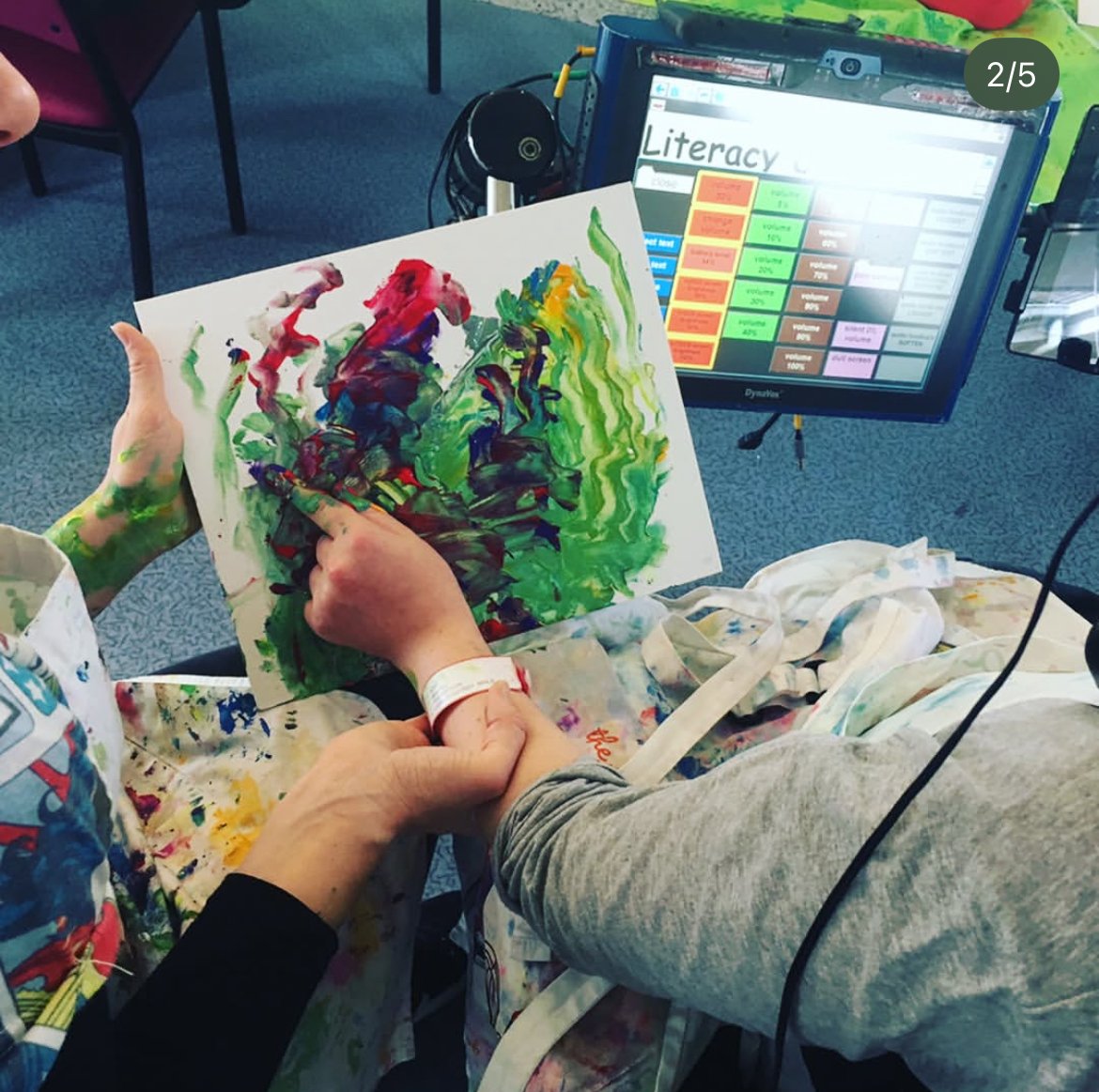 young person's hand finger painting, being support by Creative Arts Therapist. In background can see a communication device