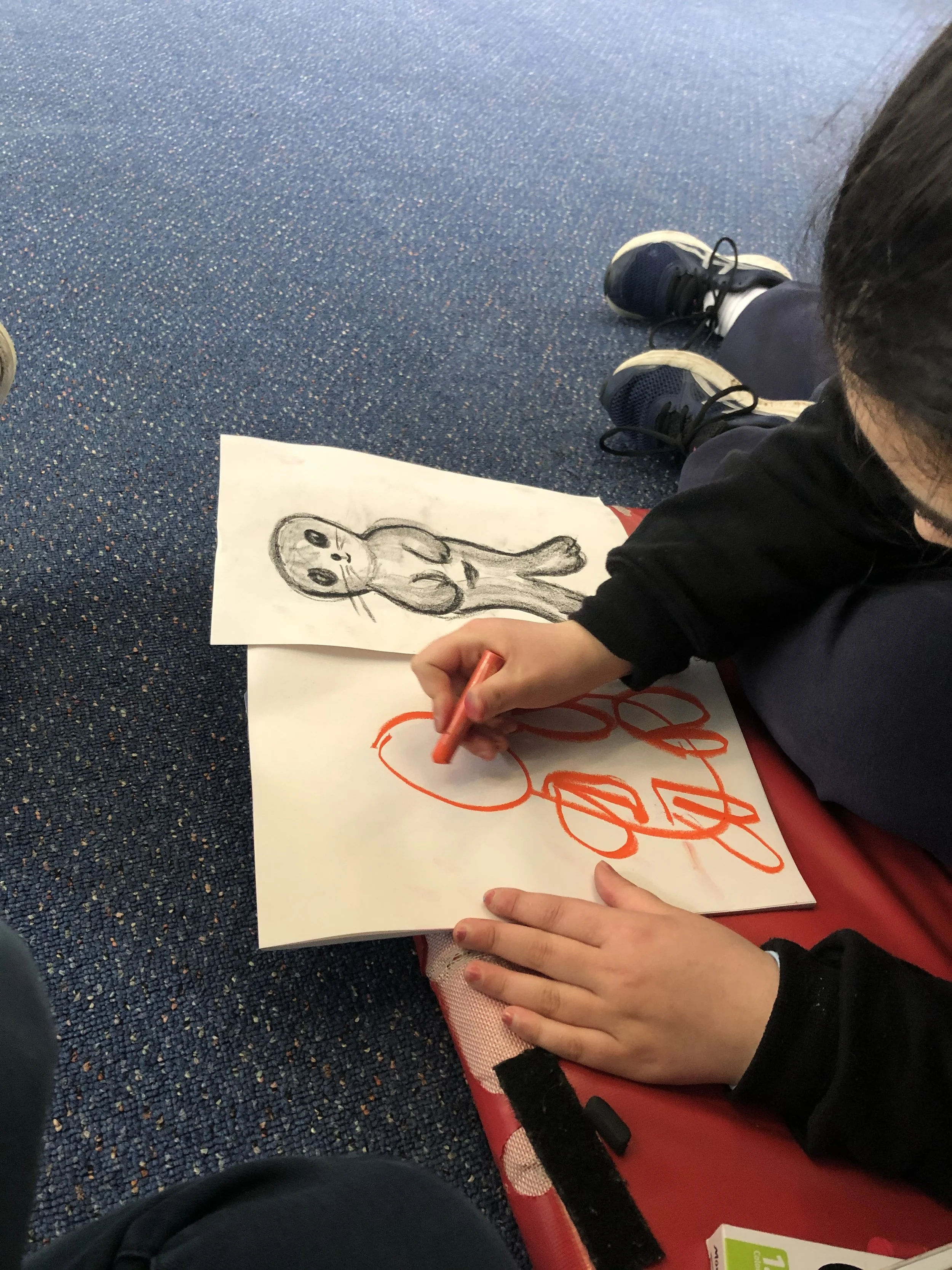young person lying on floor and copying a drawing in bright orange crayon