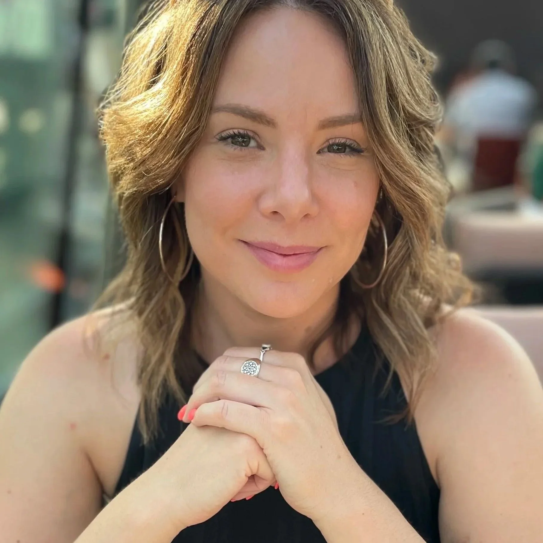 female smiling at camera with hands clasped in front of chest
