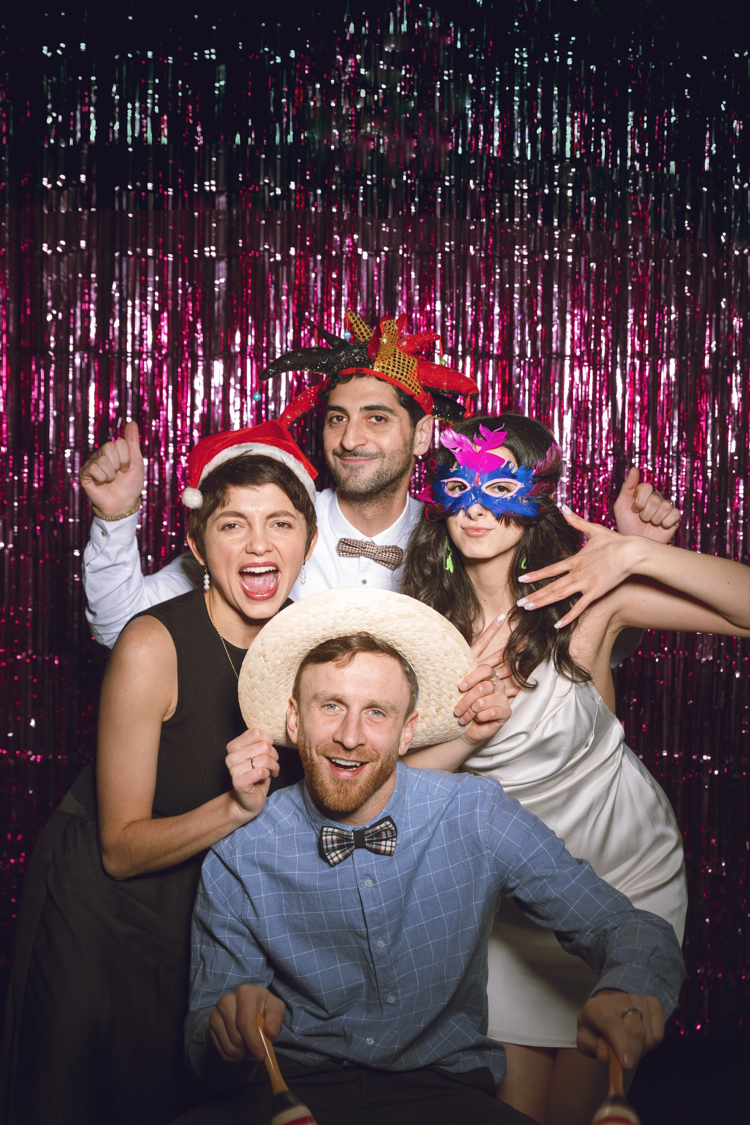 Groupe de cinq personnes joyeuses portant des accessoires de fête, posant devant un fond de décor brillant, pour une fête ou un événement festif.