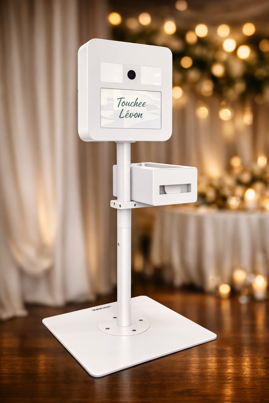 Un automate en blanc avec un écran affichant le nom 'Touchee Lévon' dans un environnement intérieur avec des lumières douces et des décorations floues en arrière-plan.