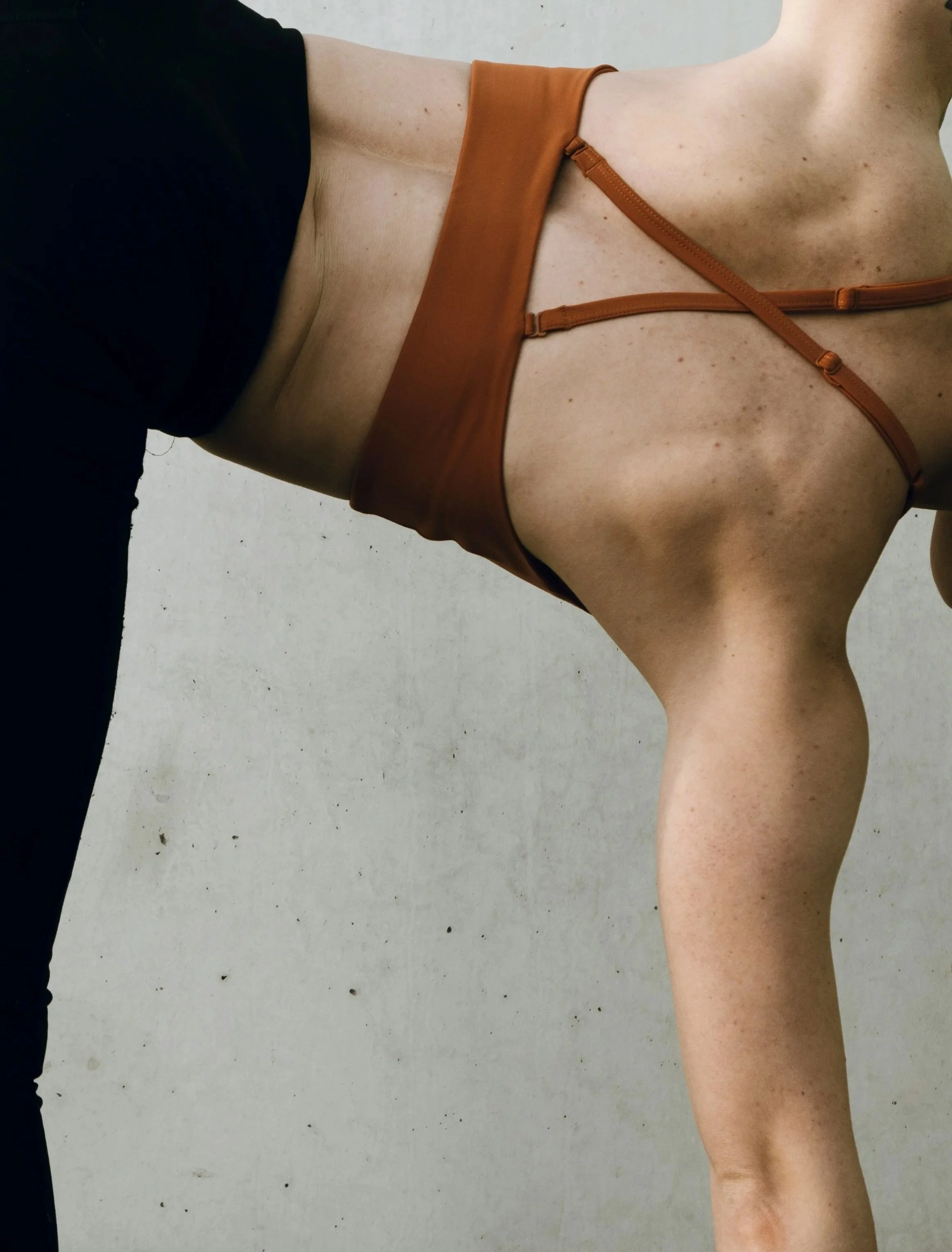 Close-up of a person's side torso, showing skin with freckles and a black shirt on the upper body, lying on a light-colored surface, with brown straps across the chest and shoulder.