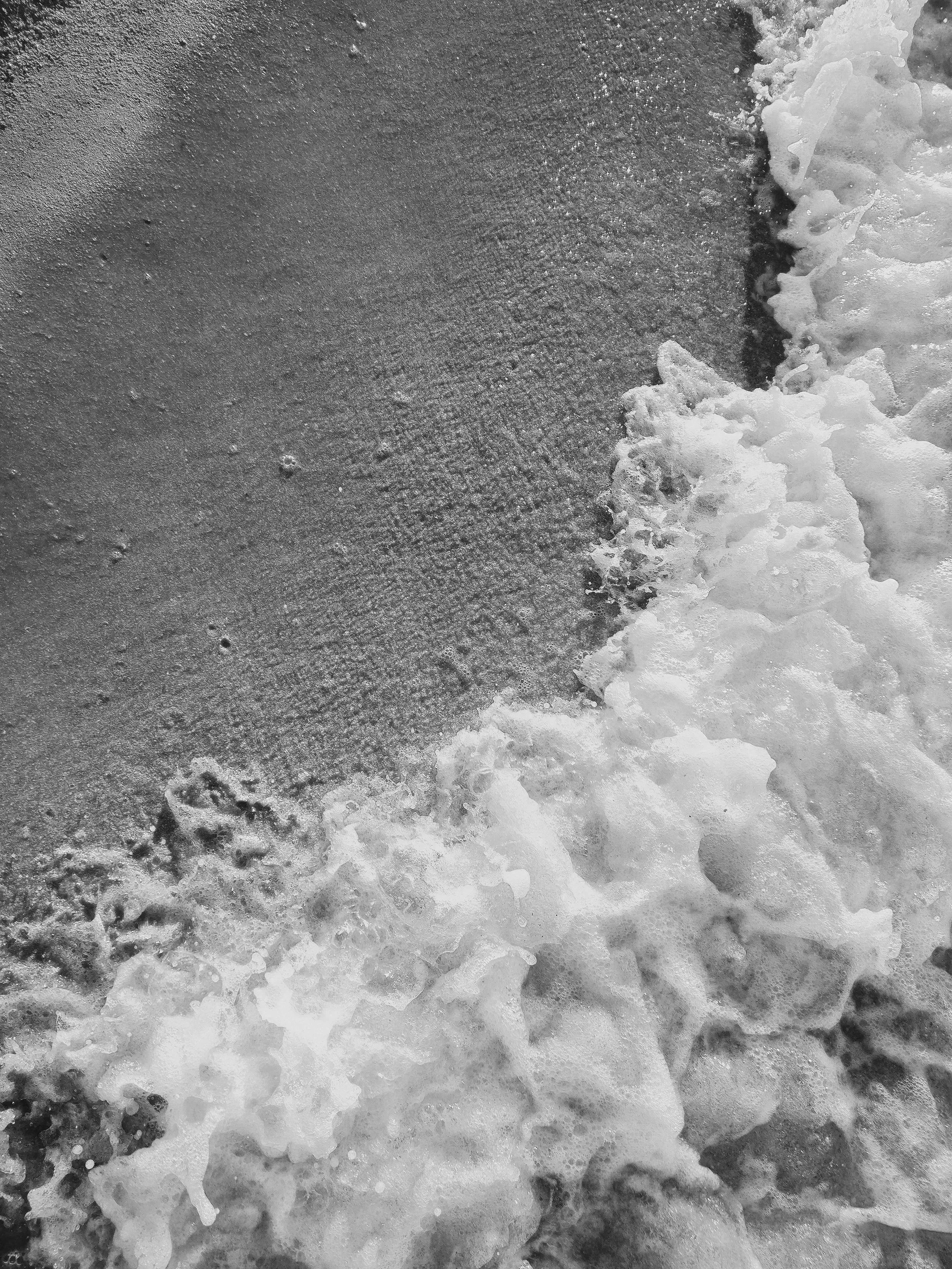 Black and white photo of ocean waves crashing onto a sandy beach.