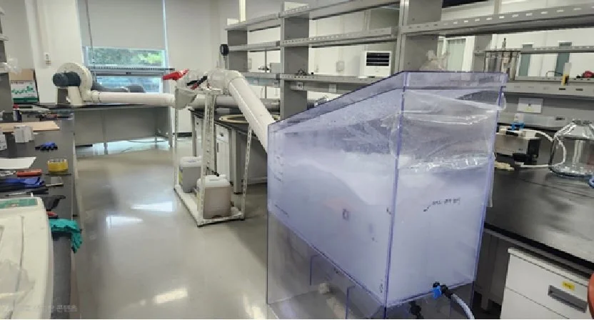 Laboratory with scientific equipment, including a large clear plastic container, a robotic arm, and various tools on countertops.