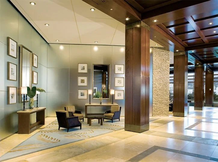 Modern hotel lobby seating area with chairs, a mirror, artwork, and wooden accents.