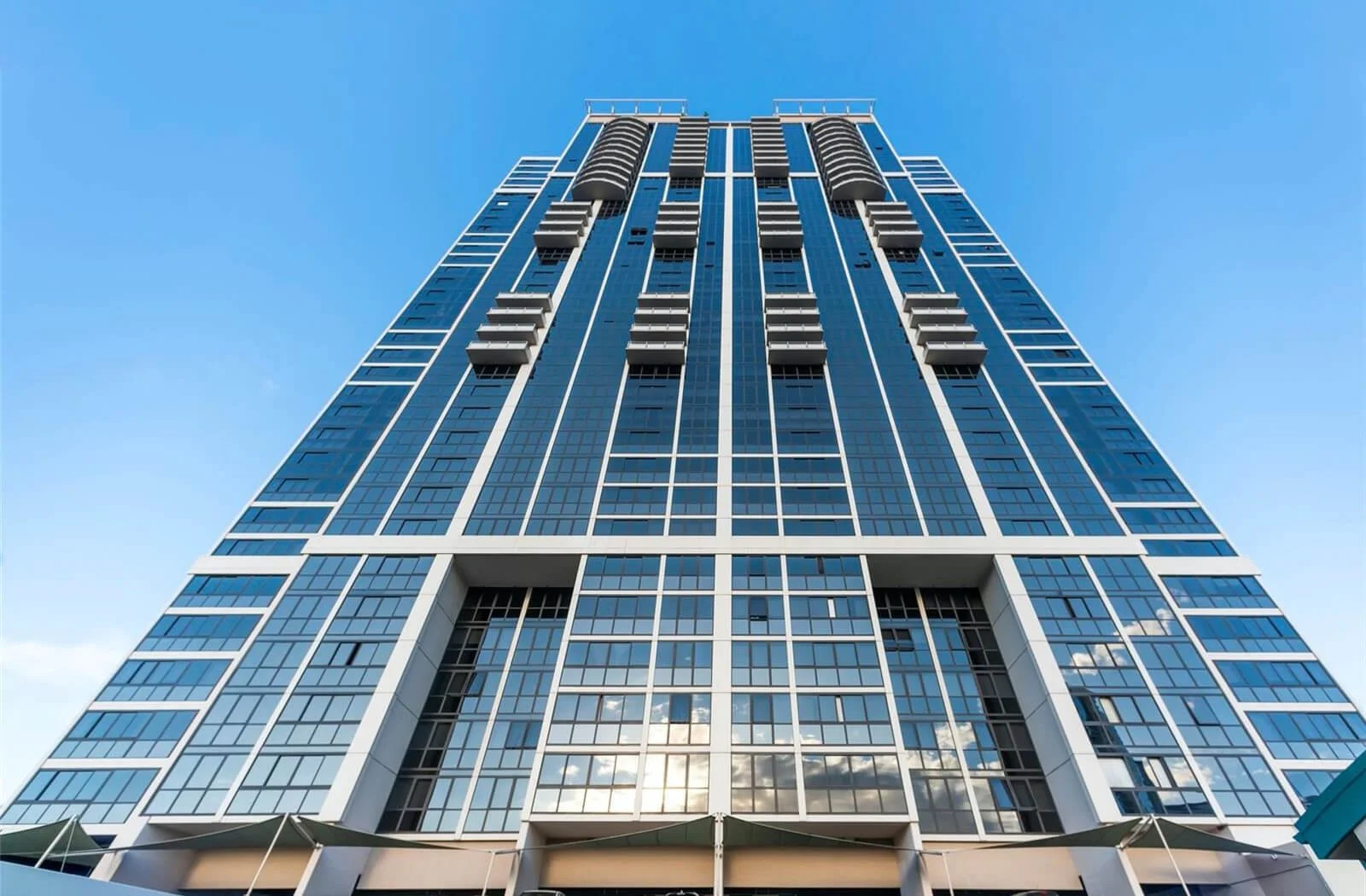 Low angle view of a tall modern glass skyscraper against a blue sky with some clouds reflected in the windows.