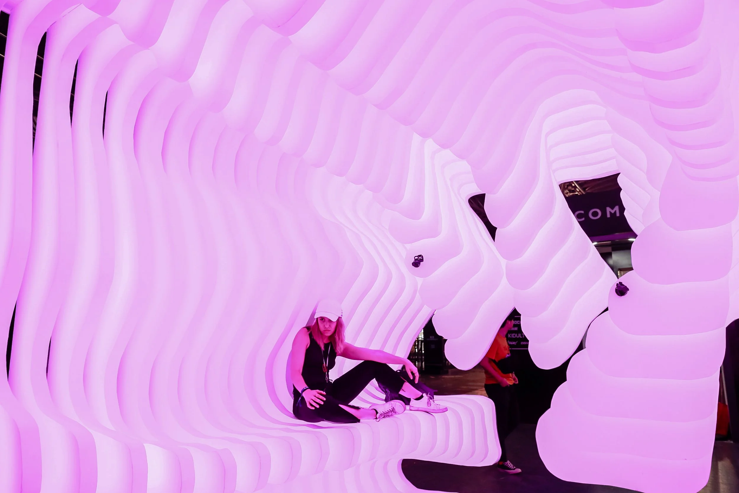 A woman sitting on a pink glowing abstract sculptural installation with wavy, layered design.