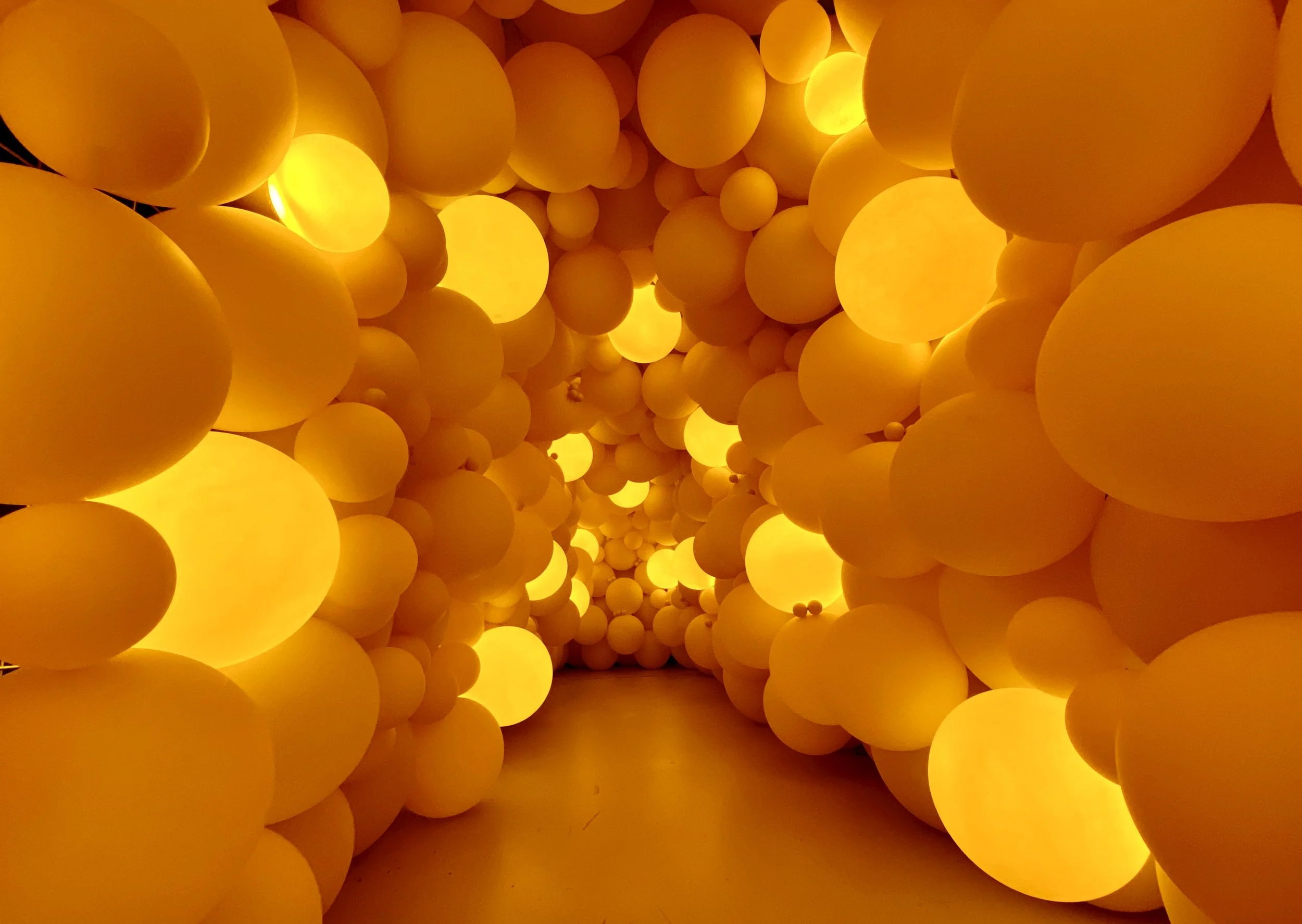 A tunnel made of numerous glowing orange and yellow spherical lights creating a warm, luminous pathway.