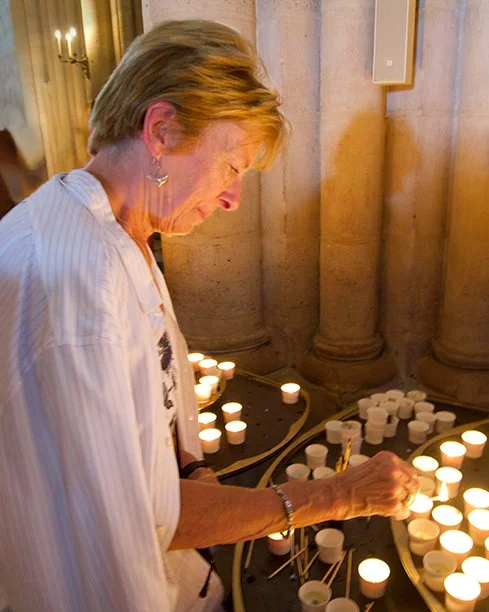 An elderly woman lighting candles on a table in a church or cathedral.