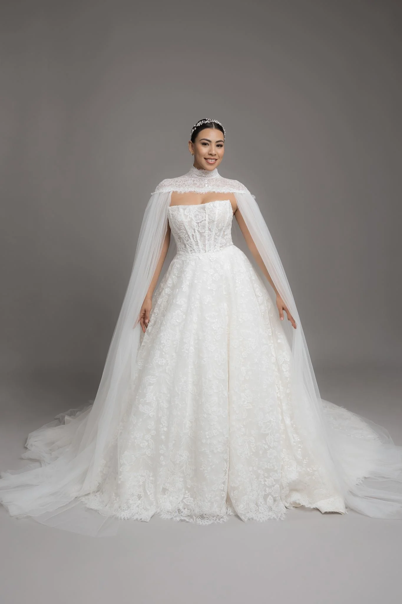 Mujer joven con vestido de novia blanco y velo, sonriendo, frente a fondo gris.