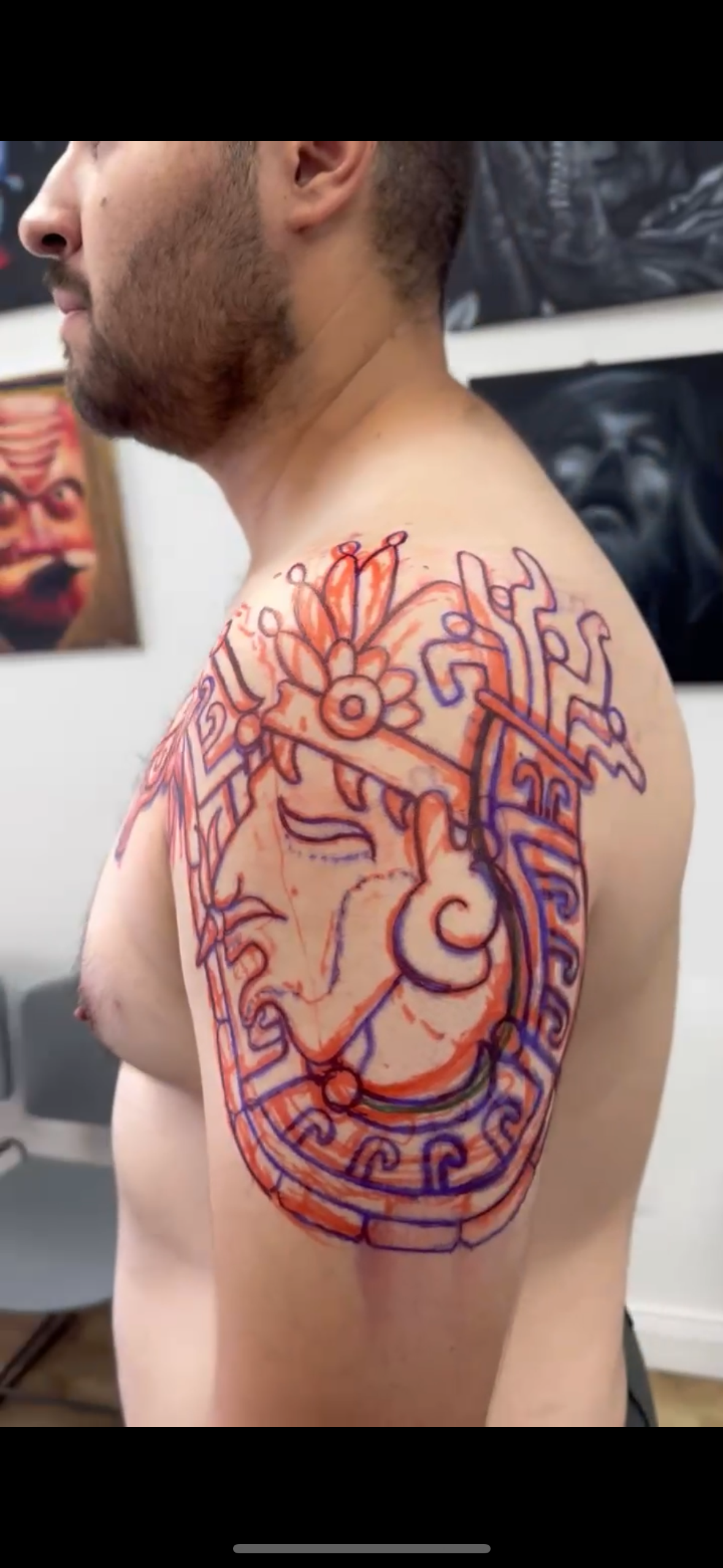 A freehand tattoo design on his shoulder and upper arm that features a Aztec face.