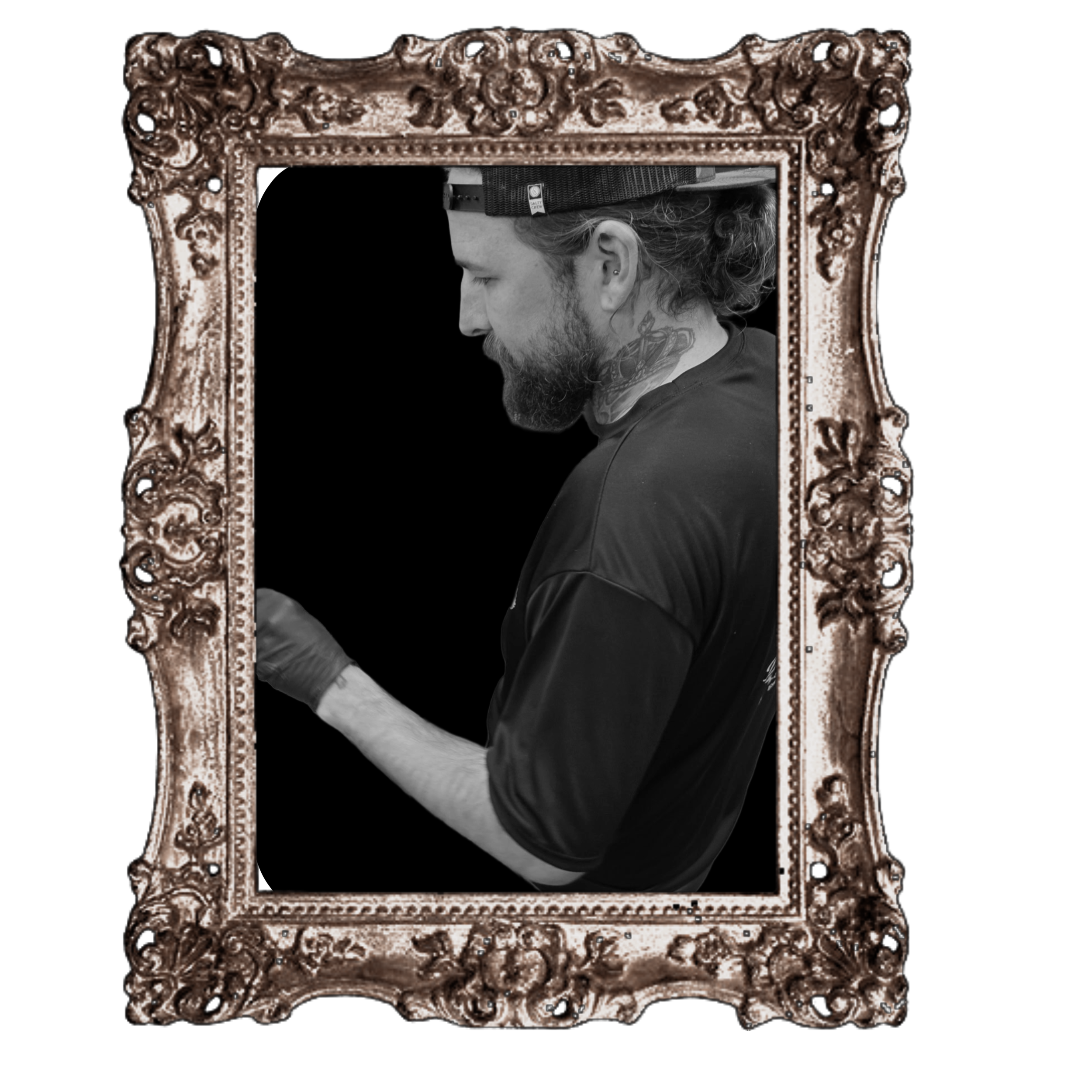 A black and white photograph of a man with a beard, tattoos, and wearing a cap, seen through an ornate, decorative picture frame with floral carvings.