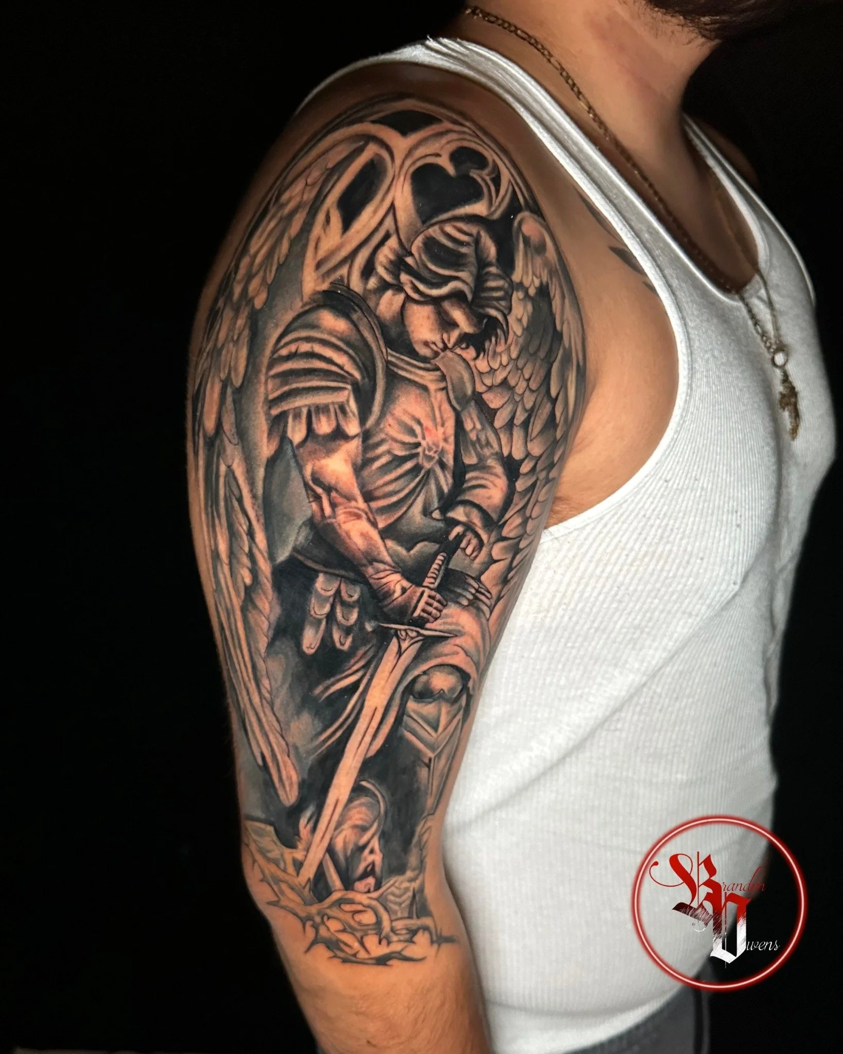 Tattoo of an angel with wings, a helmet, and a sword on a person's upper arm.