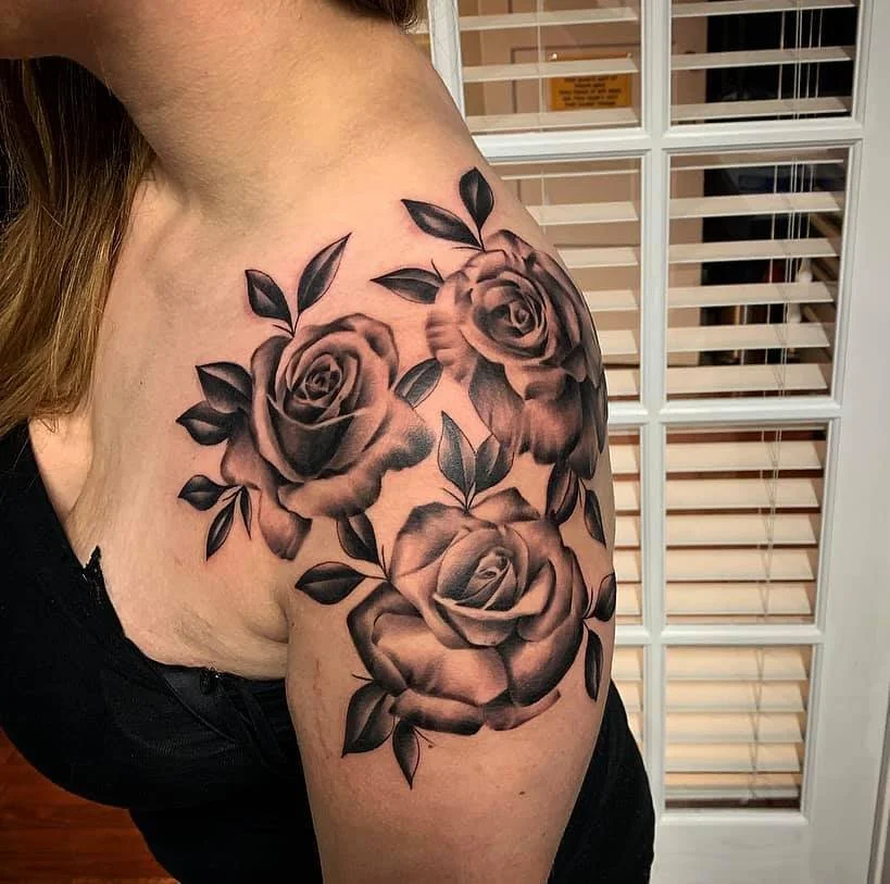 Black and gray floral tattoo of three roses with leaves on the upper arm and shoulder.