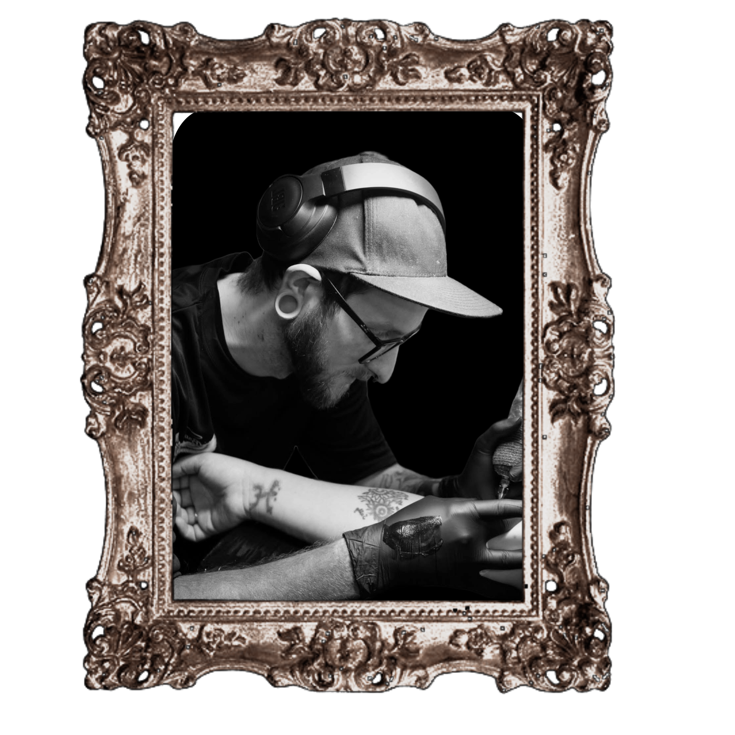Tattoo artist wearing cap, and headphones looking down, seen through an ornate, gold-colored picture frame with a black background.