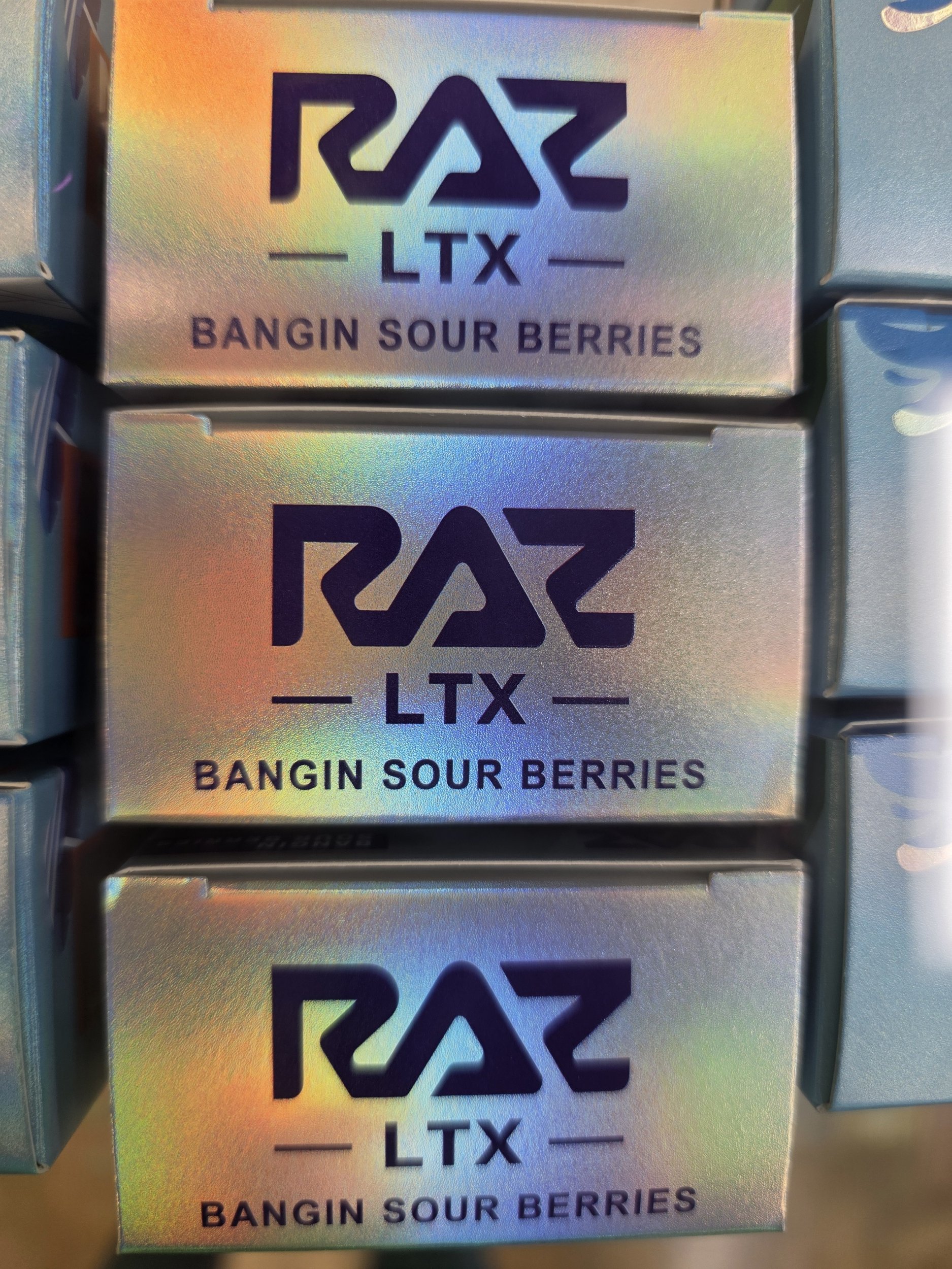 Close-up of metallic packaging with holographic sheen displaying a black logo and text that reads 'RAZ LTX' and 'BANGIN SOUR BERRIES'.