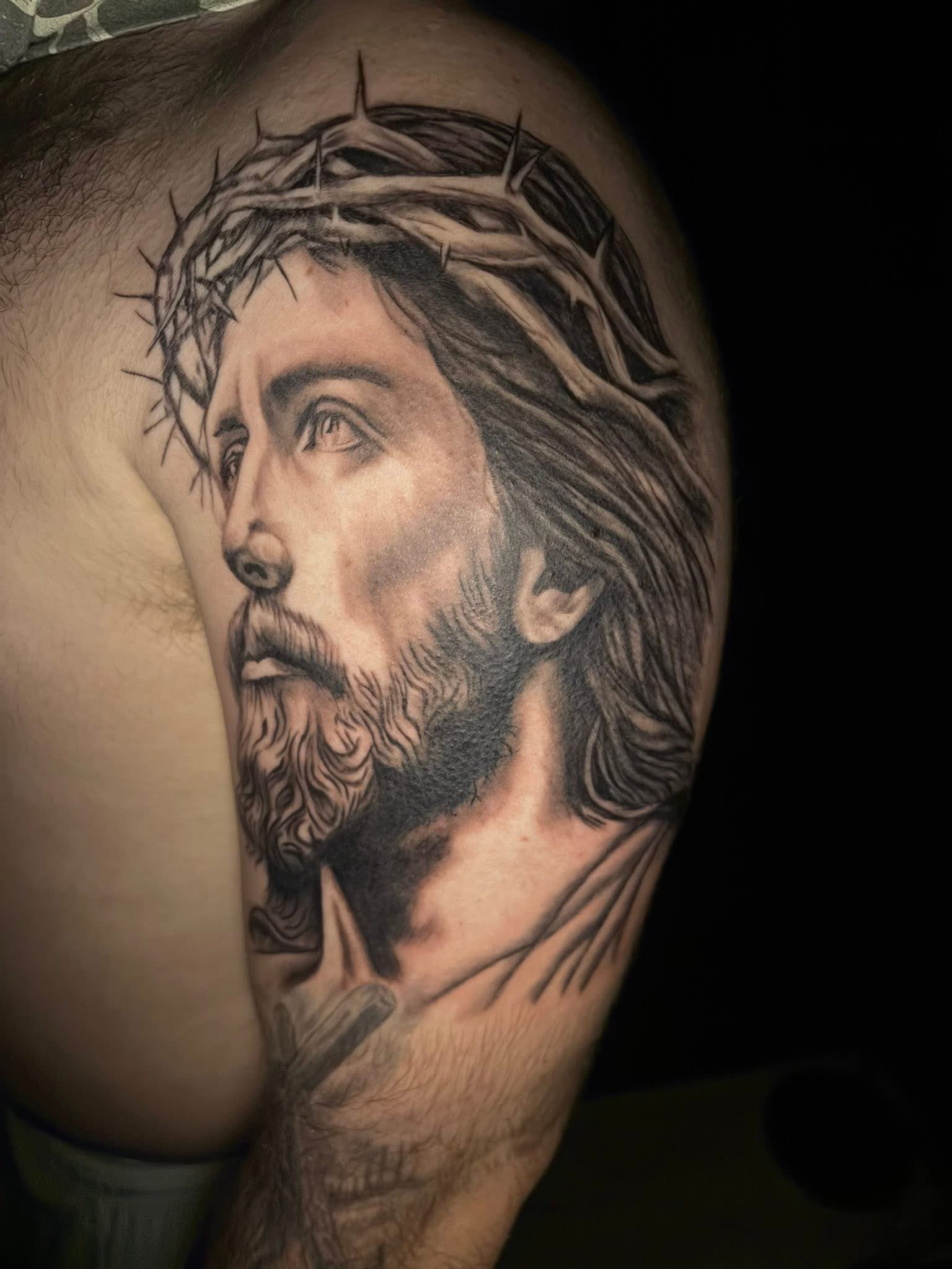 Tattoo of Jesus Christ with a crown of thorns on his head, looking upwards, on a person's upper arm.