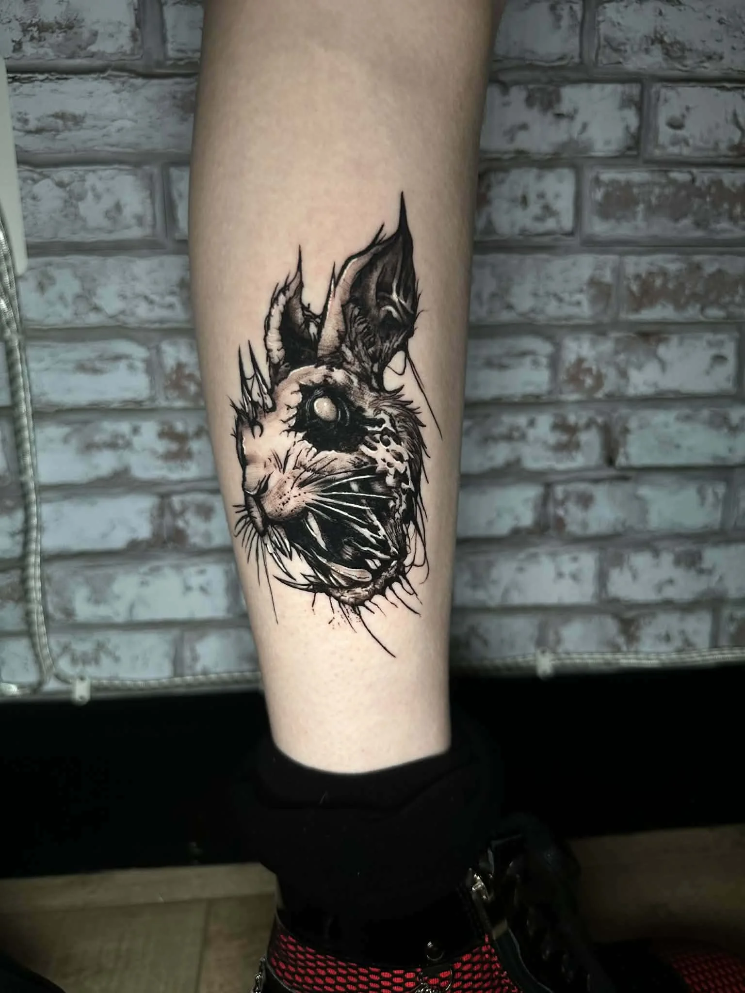 Black and gray tattoo of a cat's face on a person's calf, featuring realistic fur details and expressive eyes.