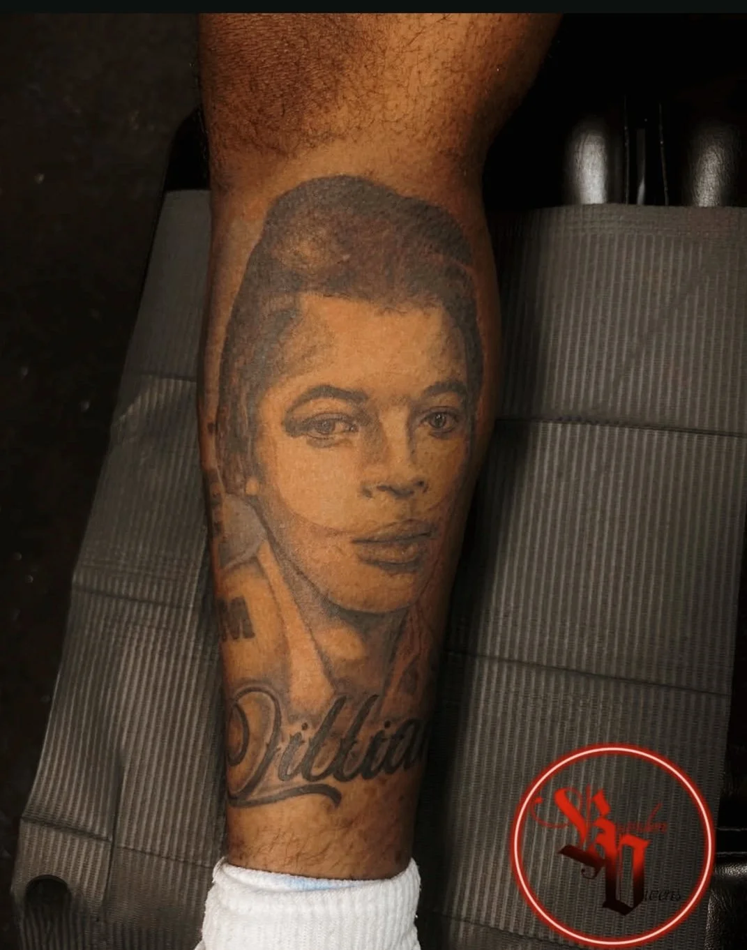 Portrait Tattoo of a young man's face with short hair and a name written in script on the lower part of the calf.