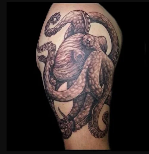 A realism tattoo of an octopus on a person's arm, featuring detailed shading and tentacles wrapped around the arm.