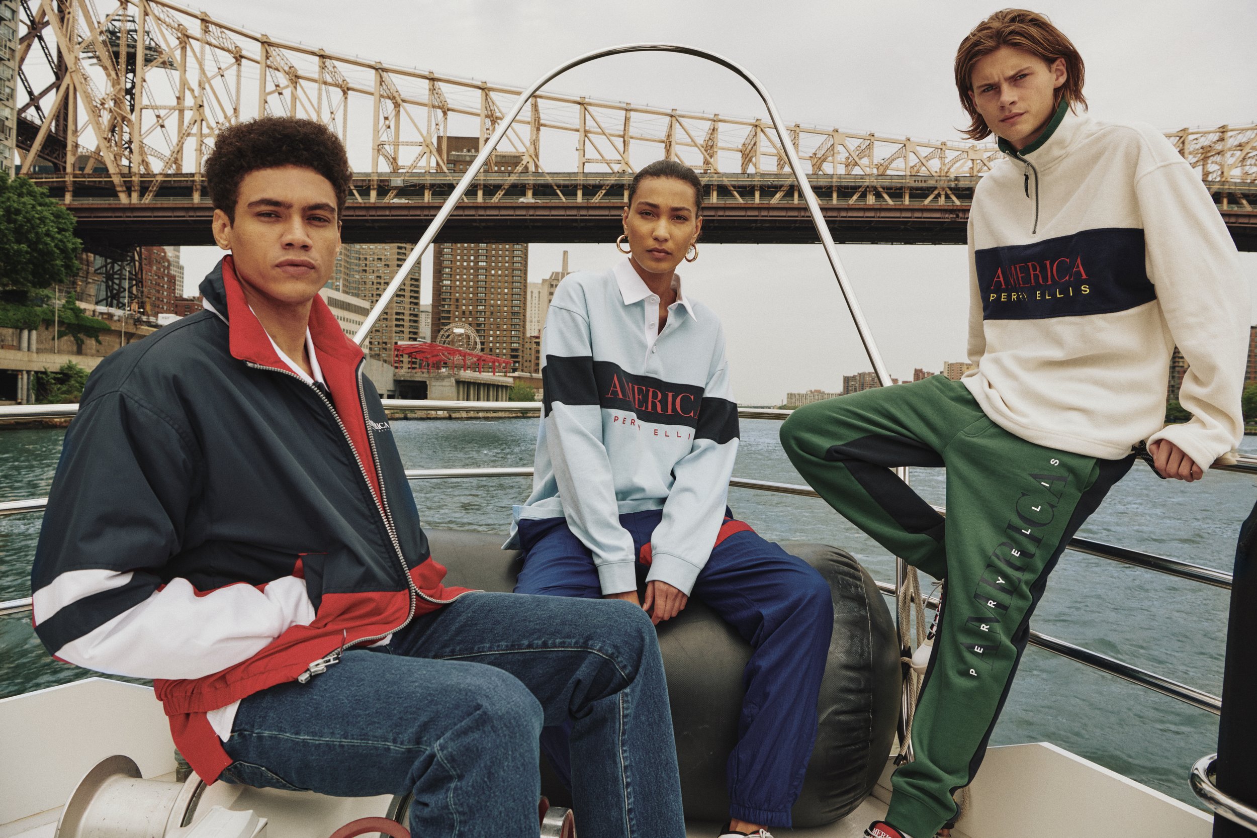 Three young adults on a boat in New York City, dressed in casual Perry Ellis clothing, with a city skyline and a bridge in the background.