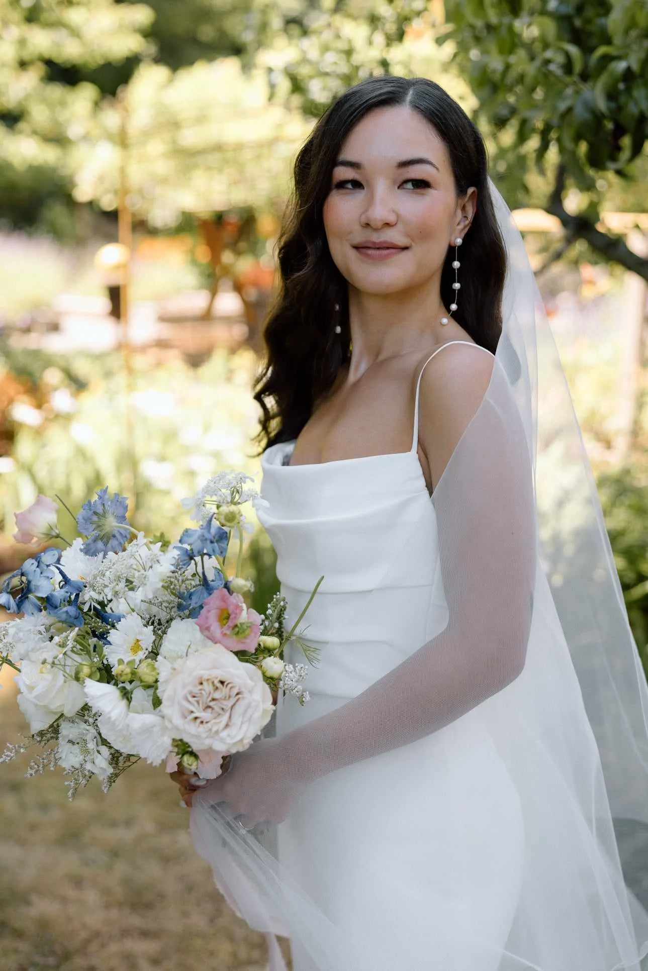 Bride in a white wedding dress holding a bouquet of flowers outdoors.