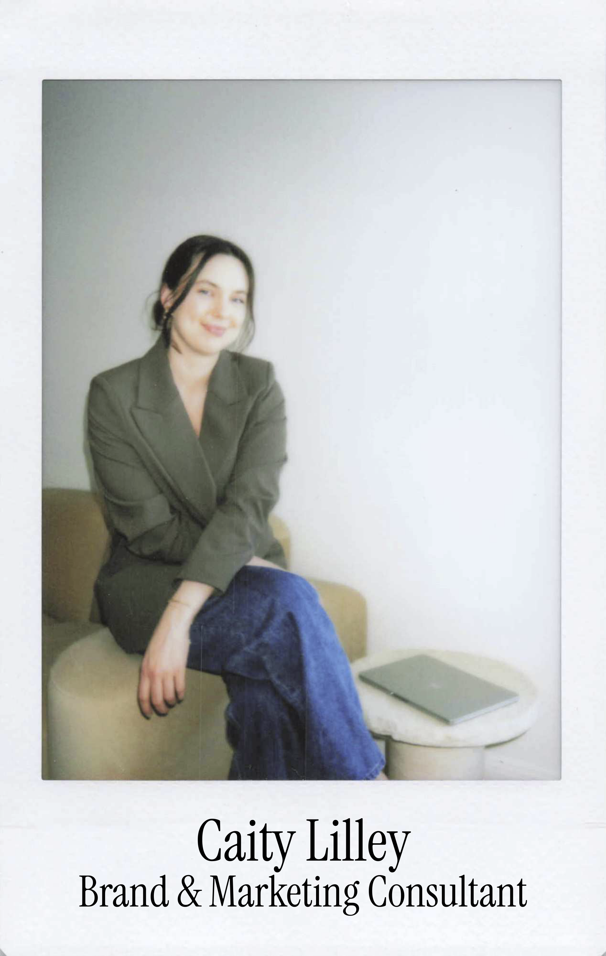 Polaroid picture of Caity Lilley, a brand and marketing consultant, sitting on a beige sofa with a closed laptop nearby, smiling at the camera.