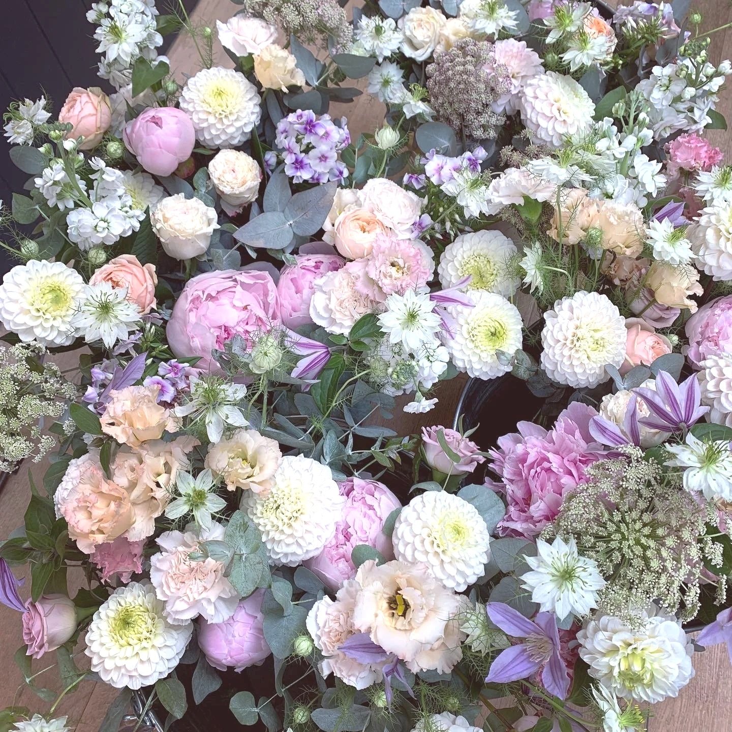 A lush arrangement of various pastel-colored flowers, including peonies, dahlias, and roses, accented with greenery and purple accents.
