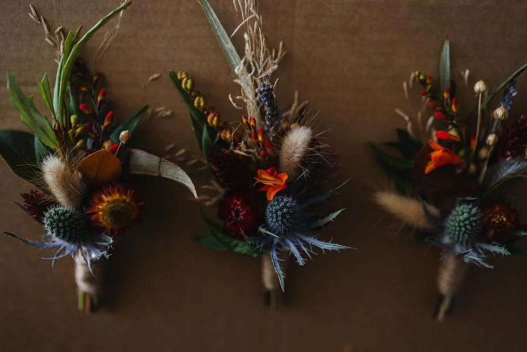 Three small floral arrangements with dried flowers and grasses on a brown background.