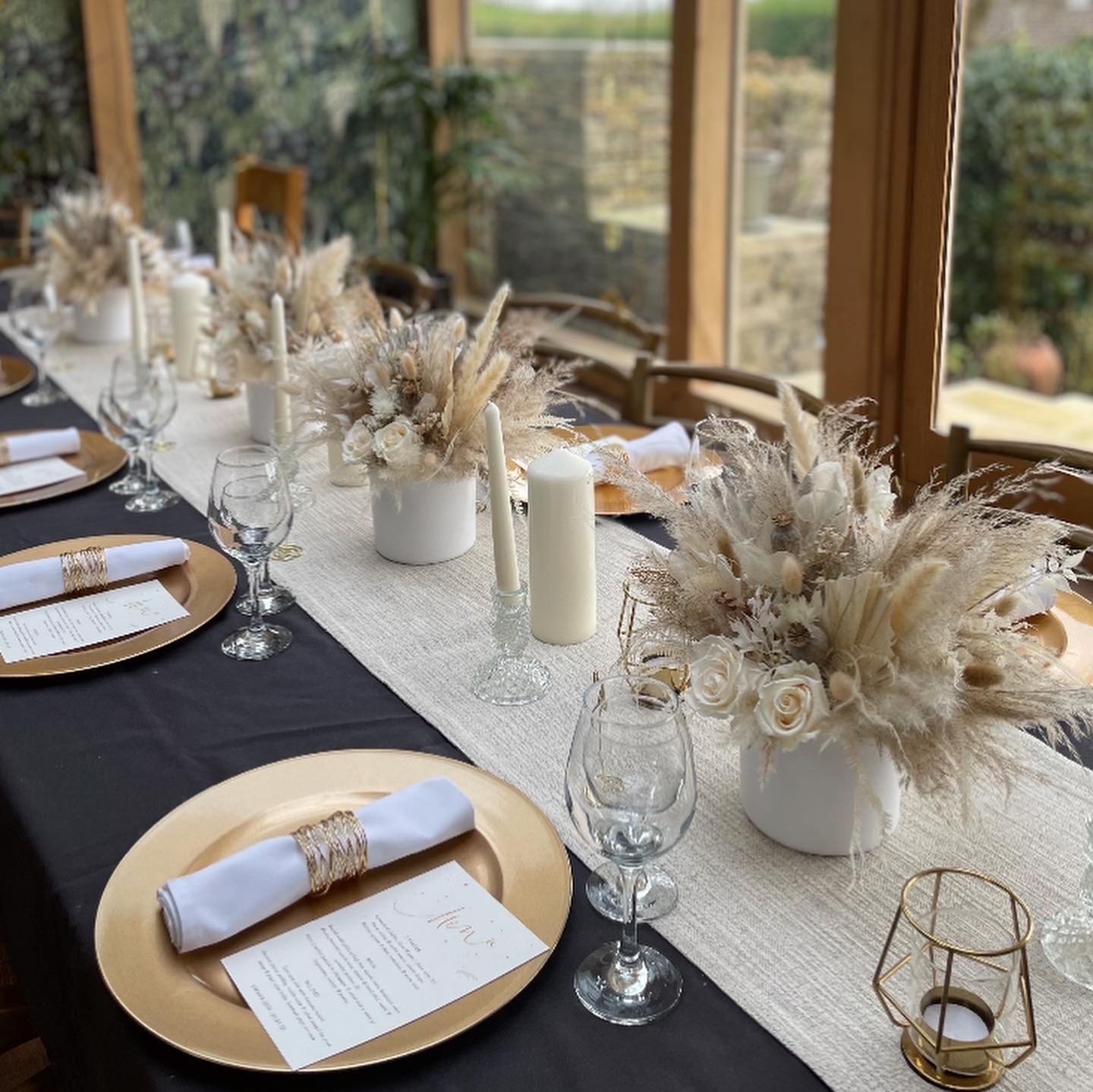 Elegant wedding or event table setup with white and gold accents, floral arrangements, candles, and place settings.