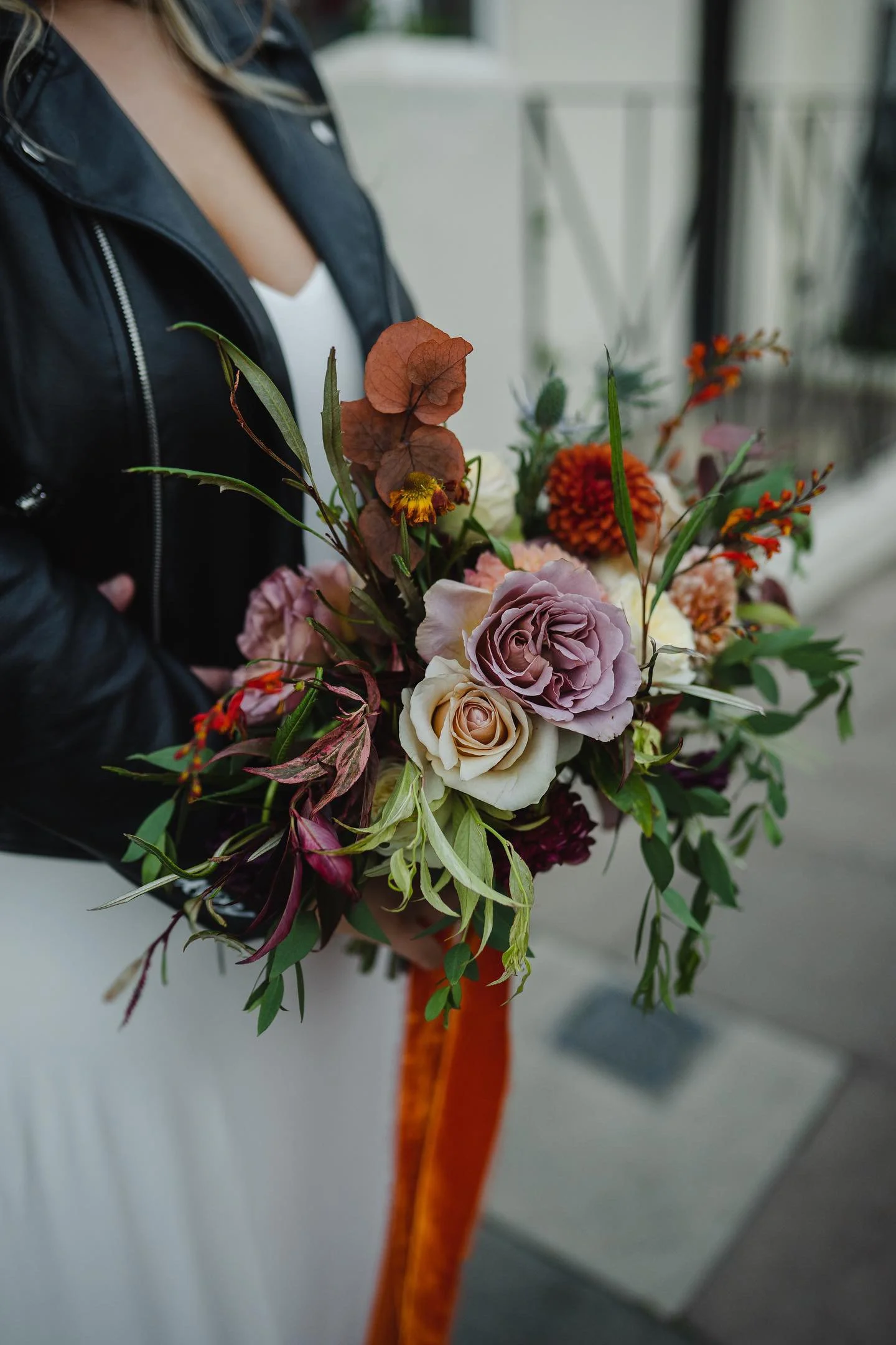 A person holding a colorful bouquet of flowers, including roses, marigolds, and various greenery, in an outdoor setting.