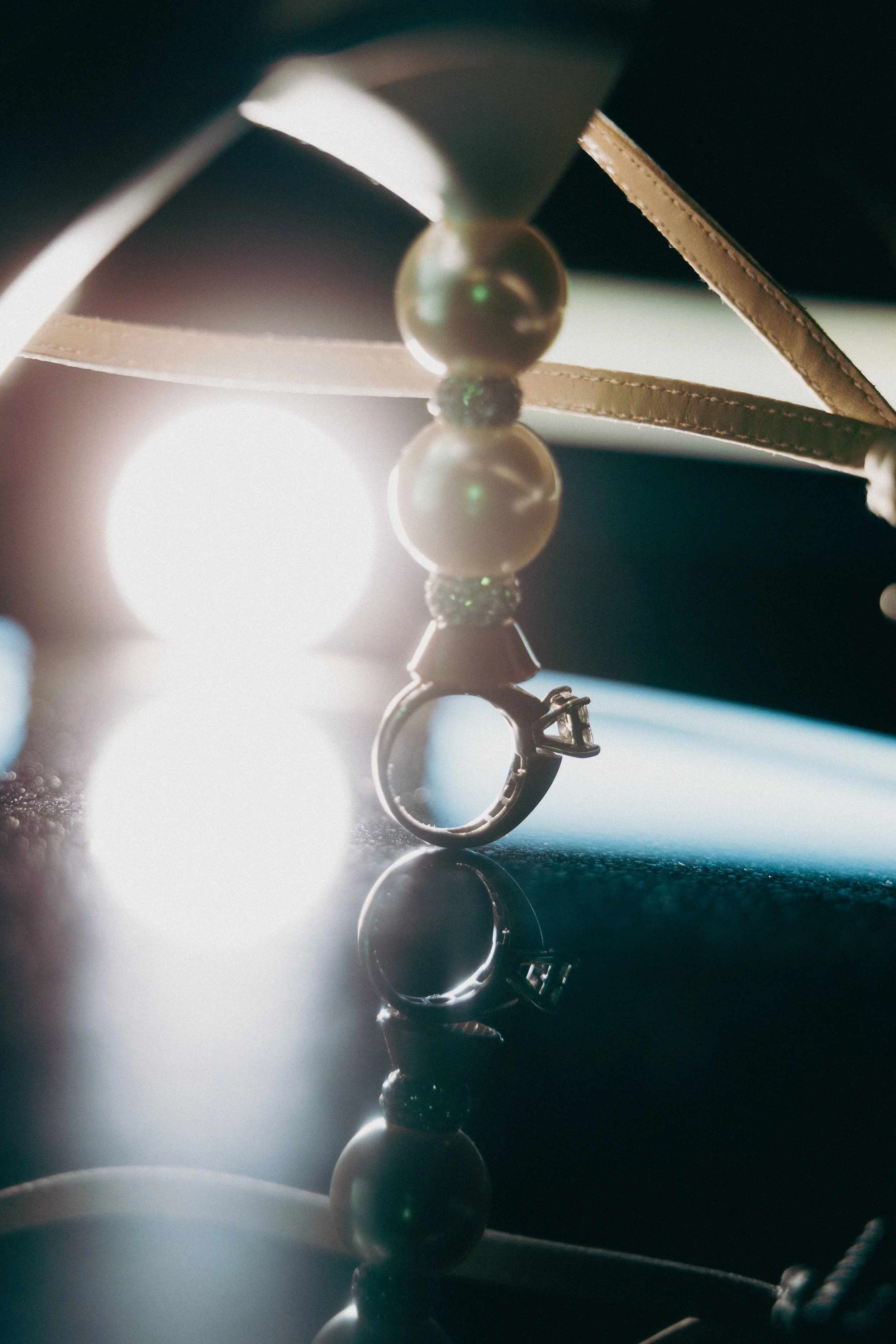 A close-up shot of a ring with a butterfly-shaped top, including beads and leather straps, illuminated with backlighting, creating reflections and a glowing effect.
