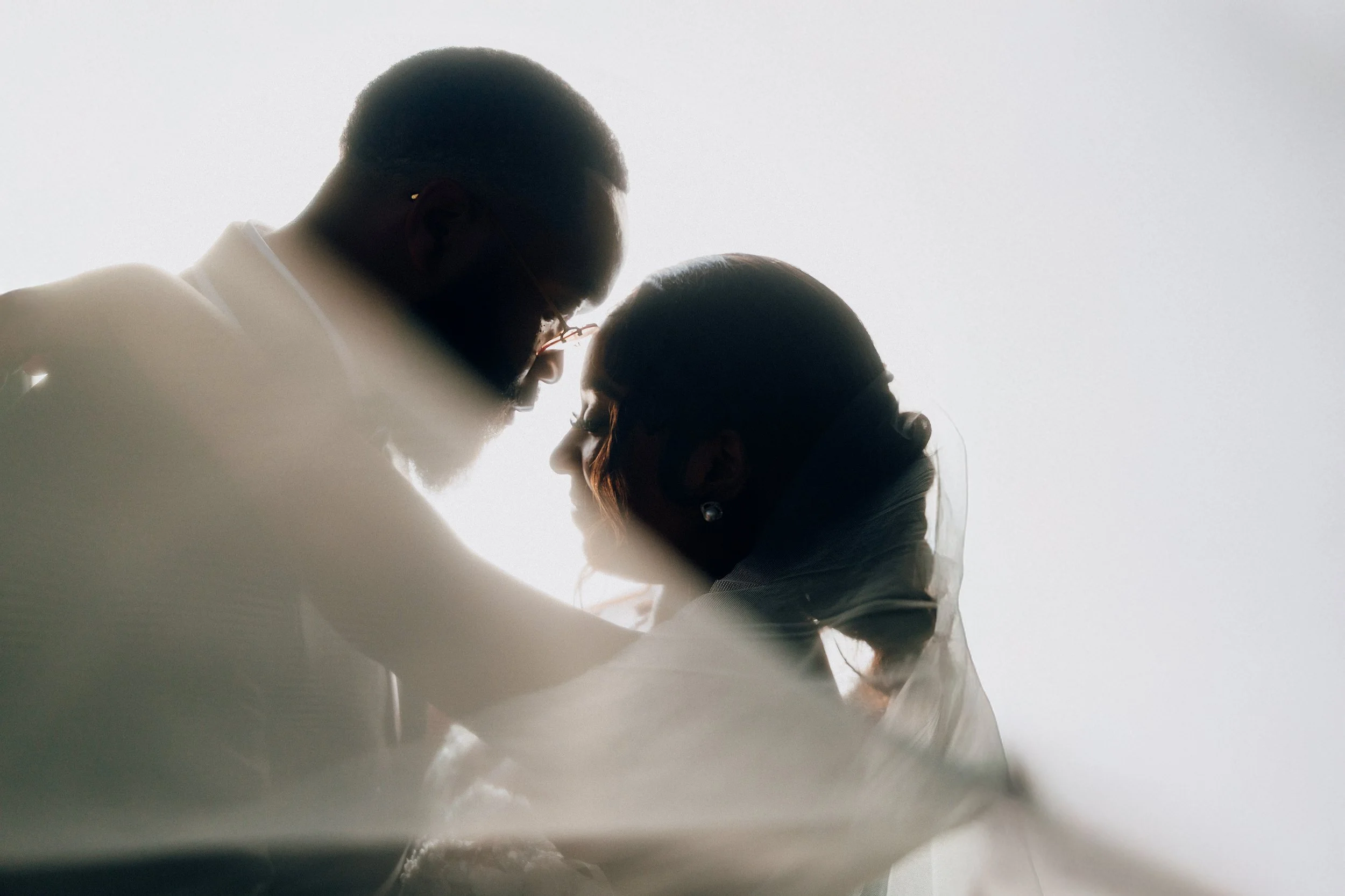 A silhouette of a man and woman facing each other, close together, with light coming behind them creating a backlit effect.