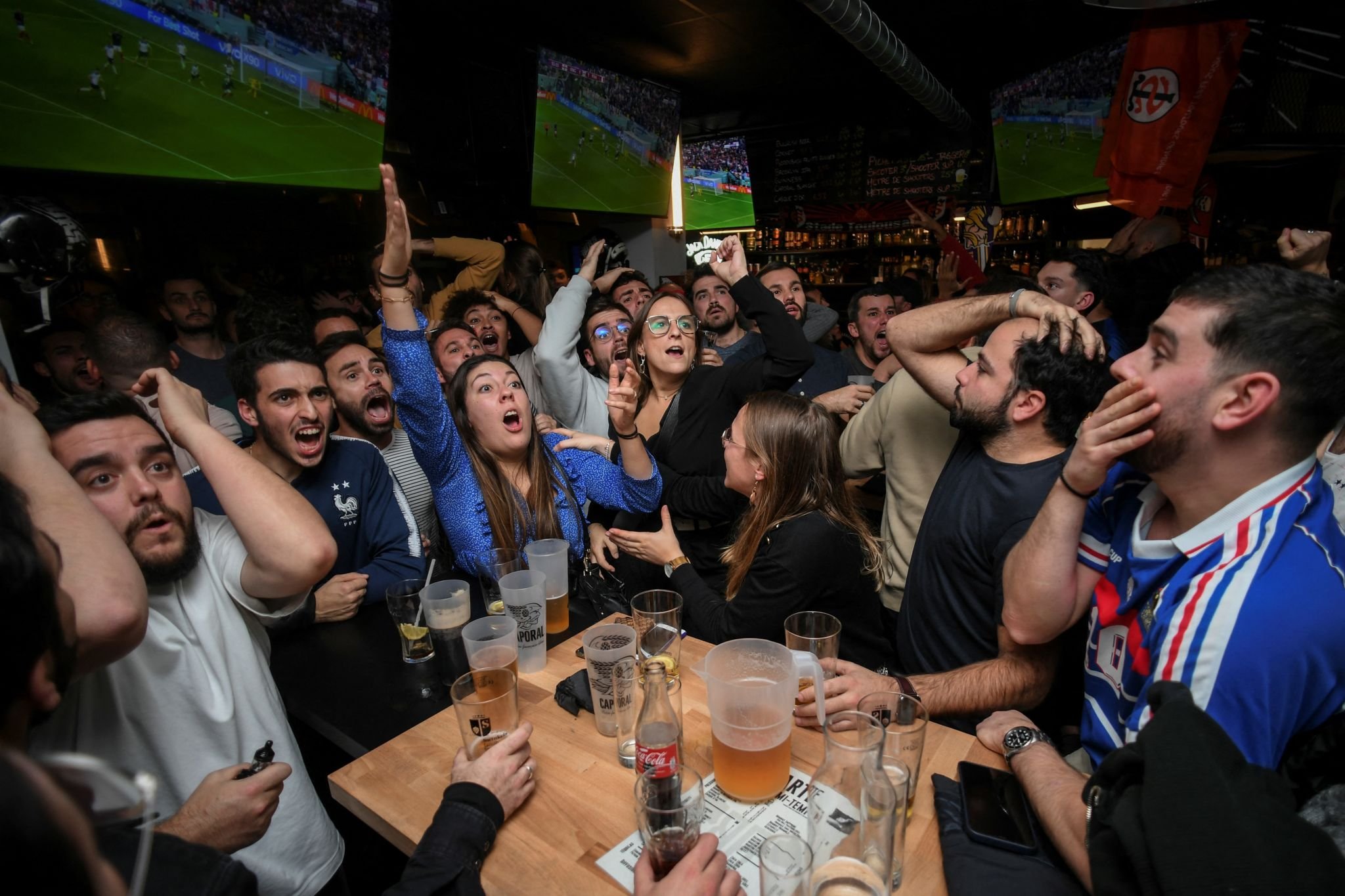 A group of people at a bar watching a soccer match on TV, appearing excited and animated.