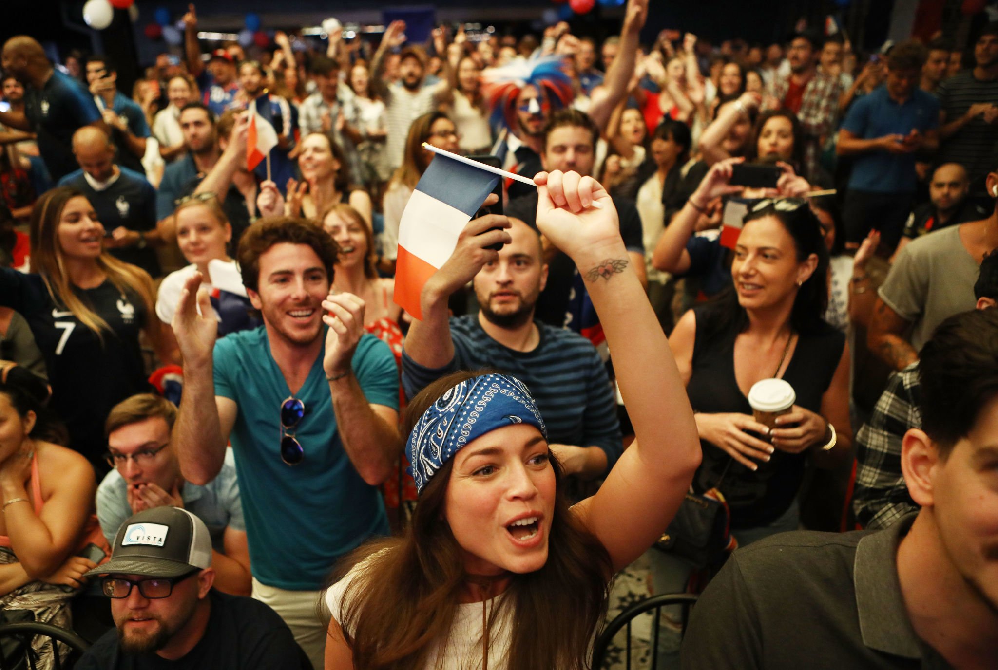 Crowd of people celebrating at a sporting event, many holding and waving French flags, with smiling faces and enthusiastic expressions.