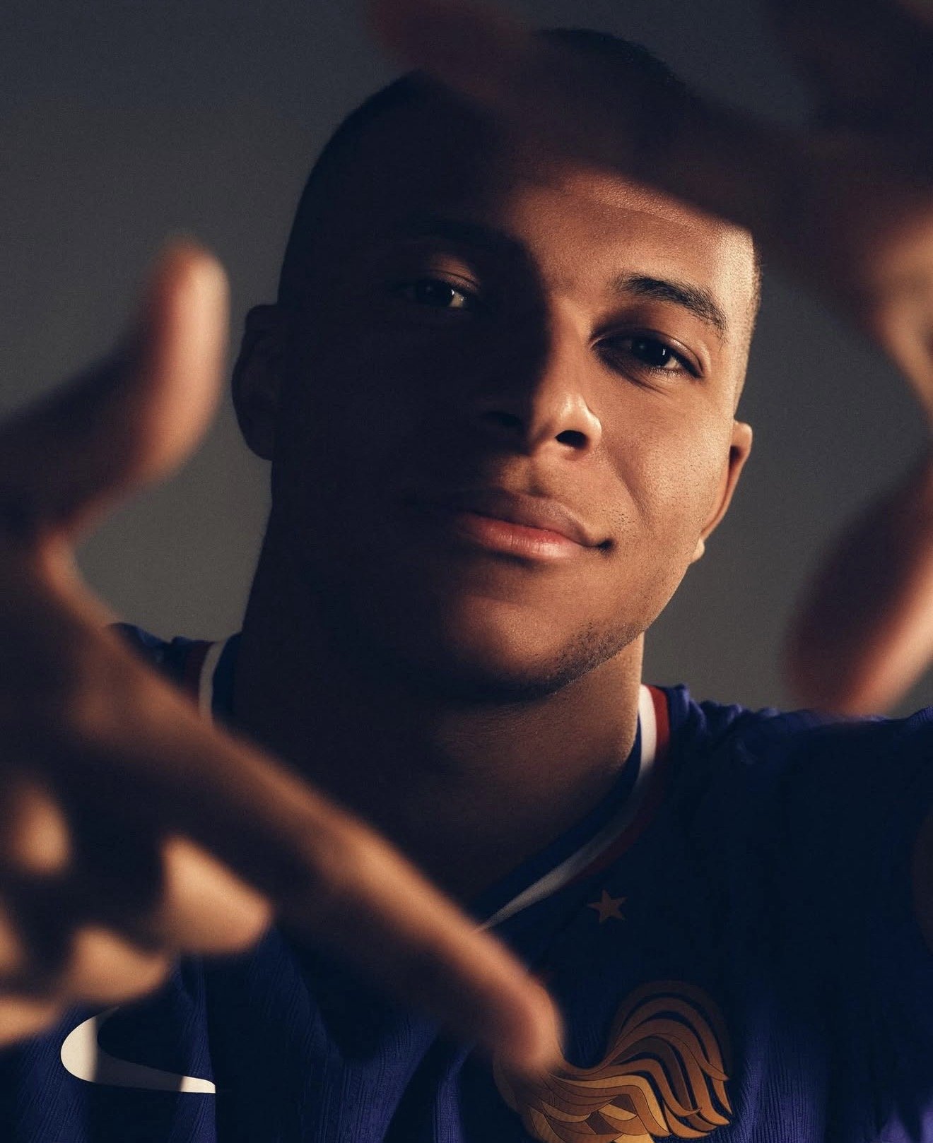 Close-up of a young man with short hair, smiling, wearing a sports jersey with a lion emblem, and making a framing gesture with his hands.