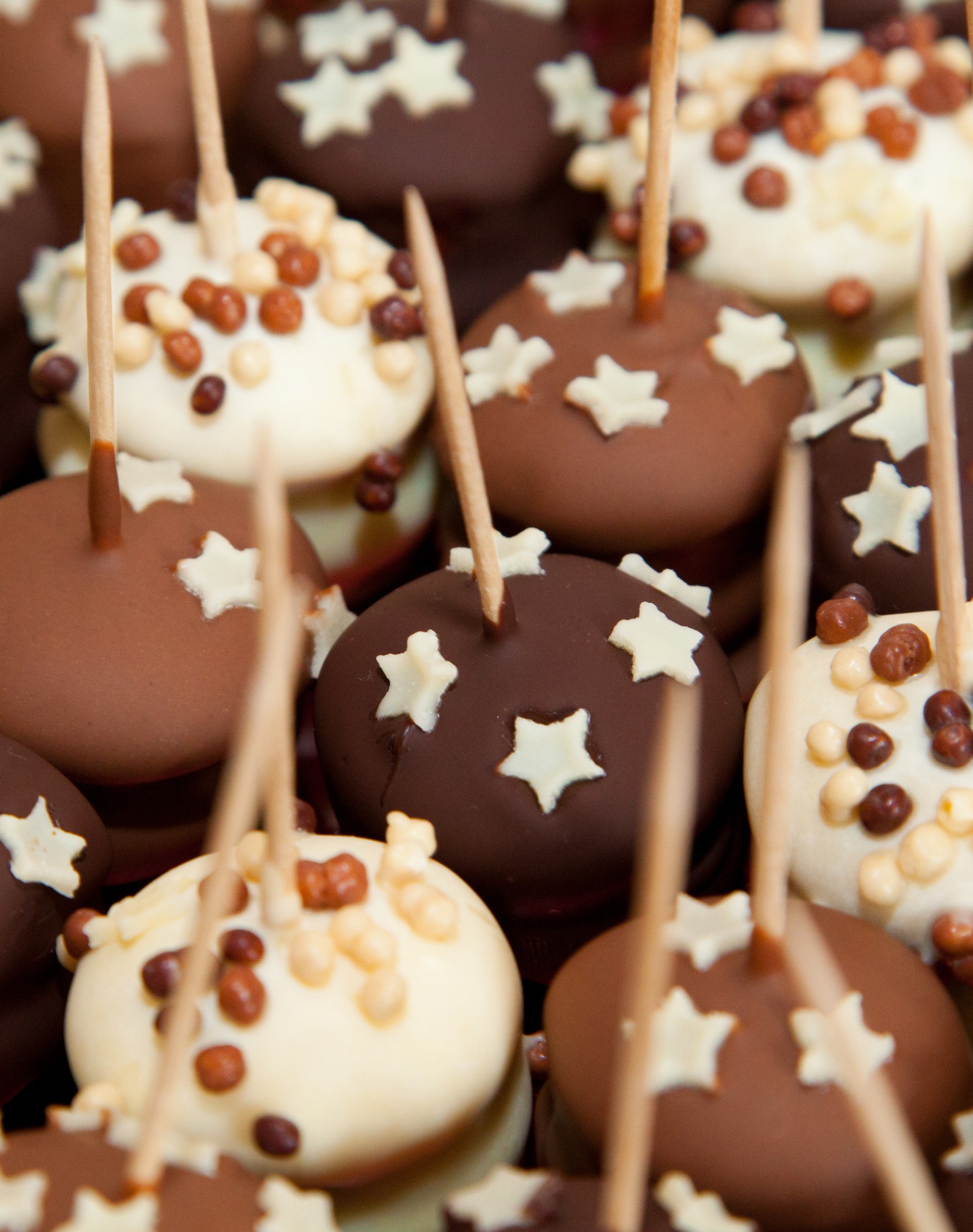 Close-up of cake pops decorated with star-shaped and small round sprinkles, in various shades of white, milk, and dark chocolate.