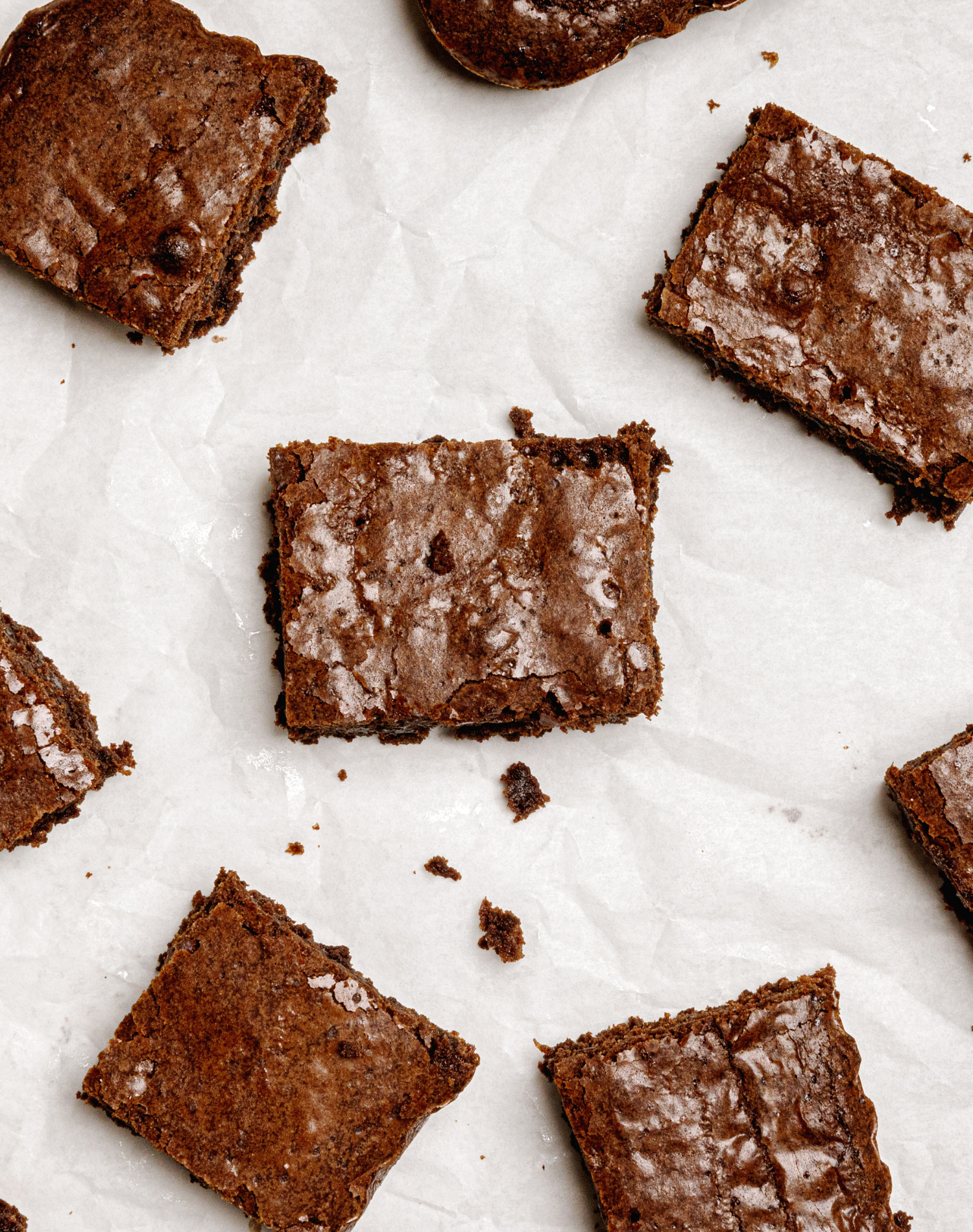 Sliced and whole chocolate brownies on white parchment paper.