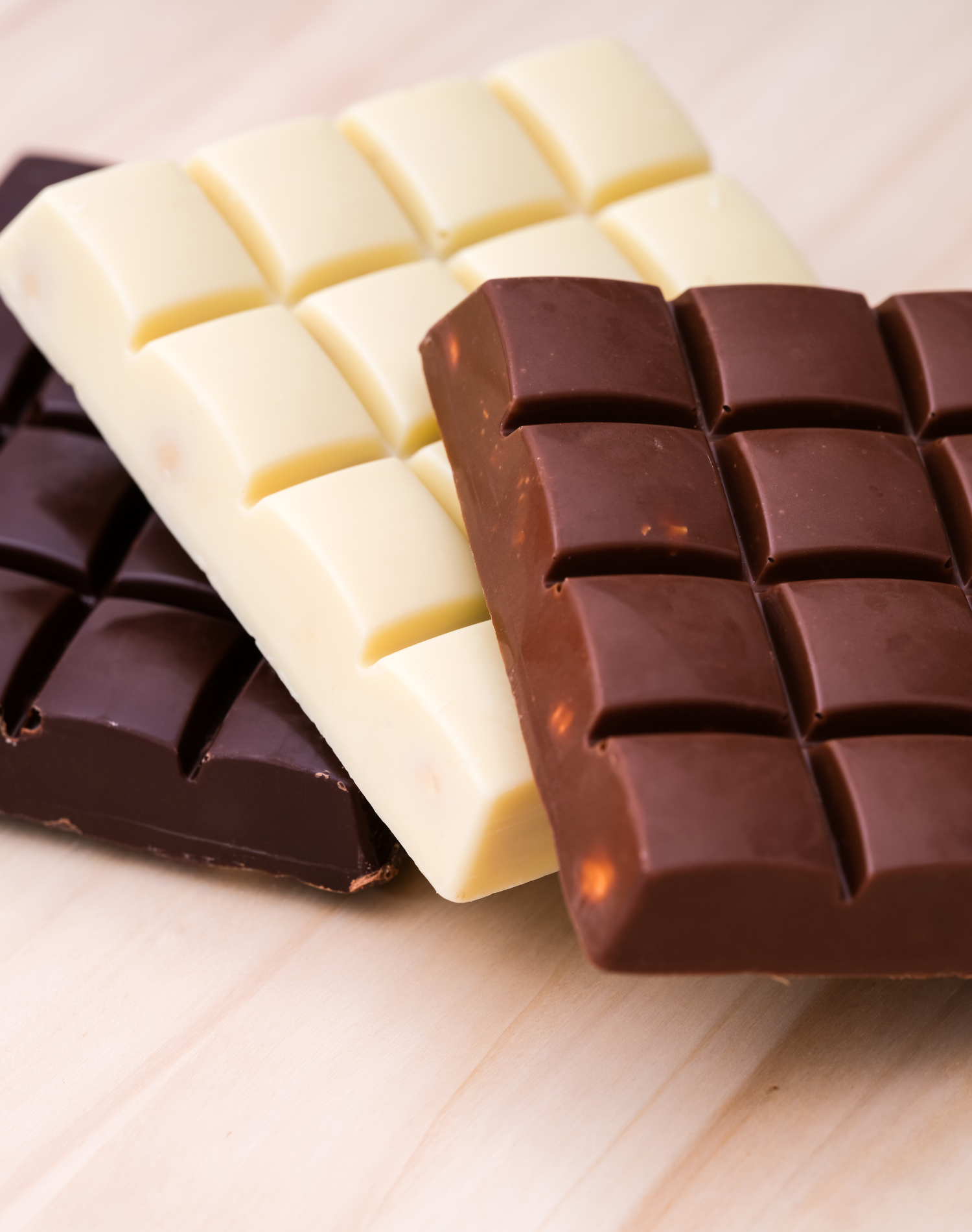 Three pieces of chocolate bars in white, milk, and dark chocolate varieties on a wooden surface.