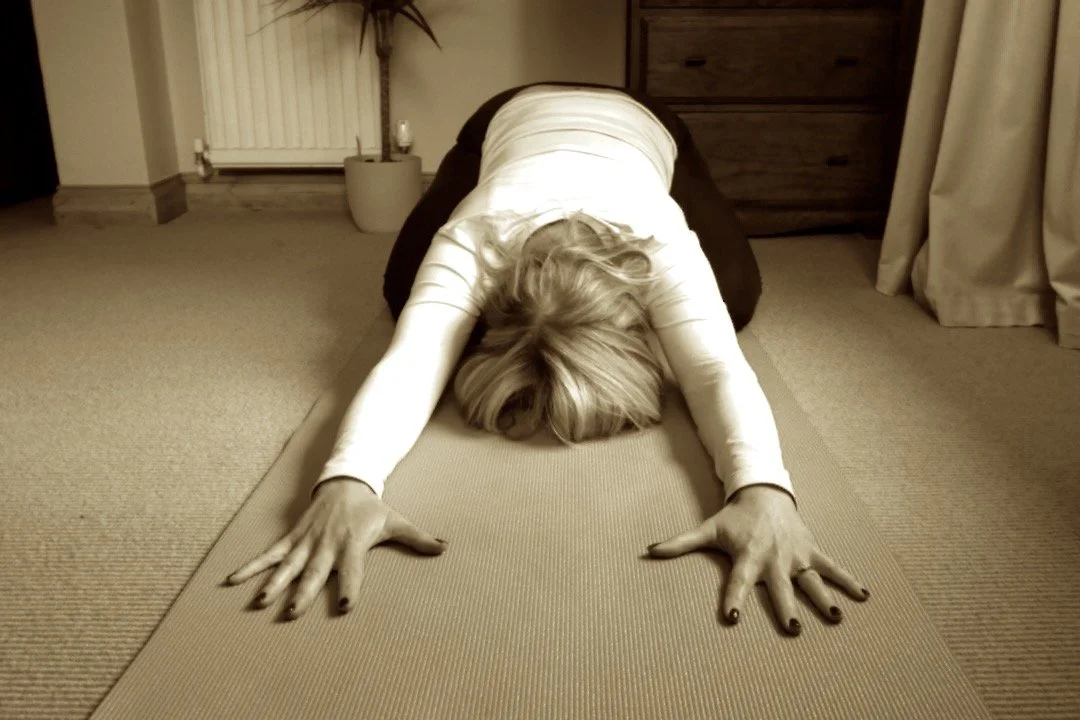 Woman practicing yoga in child's pose on yoga mat in a cozy living room.
