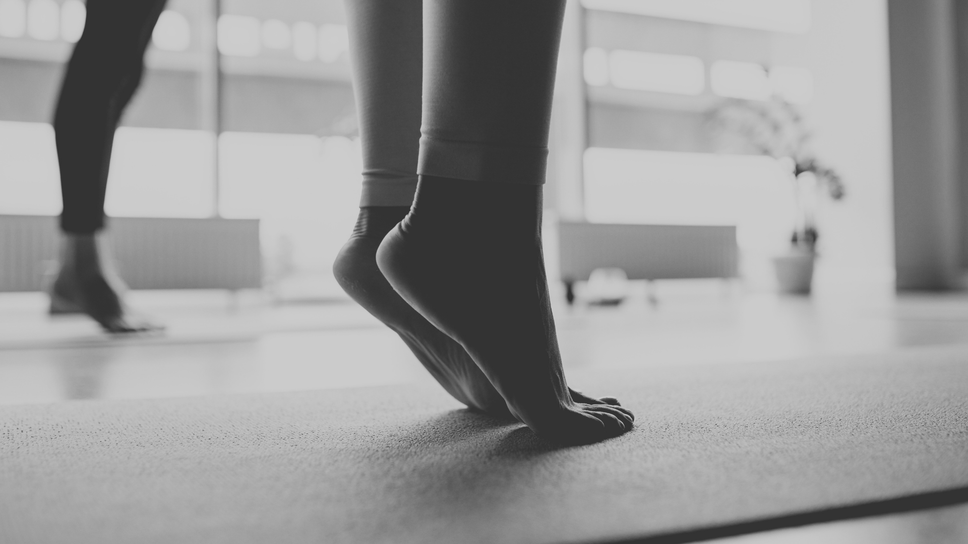 Close-up of a person in yoga pose, on a mat, with other individuals practicing yoga in mirror reflections in the background.