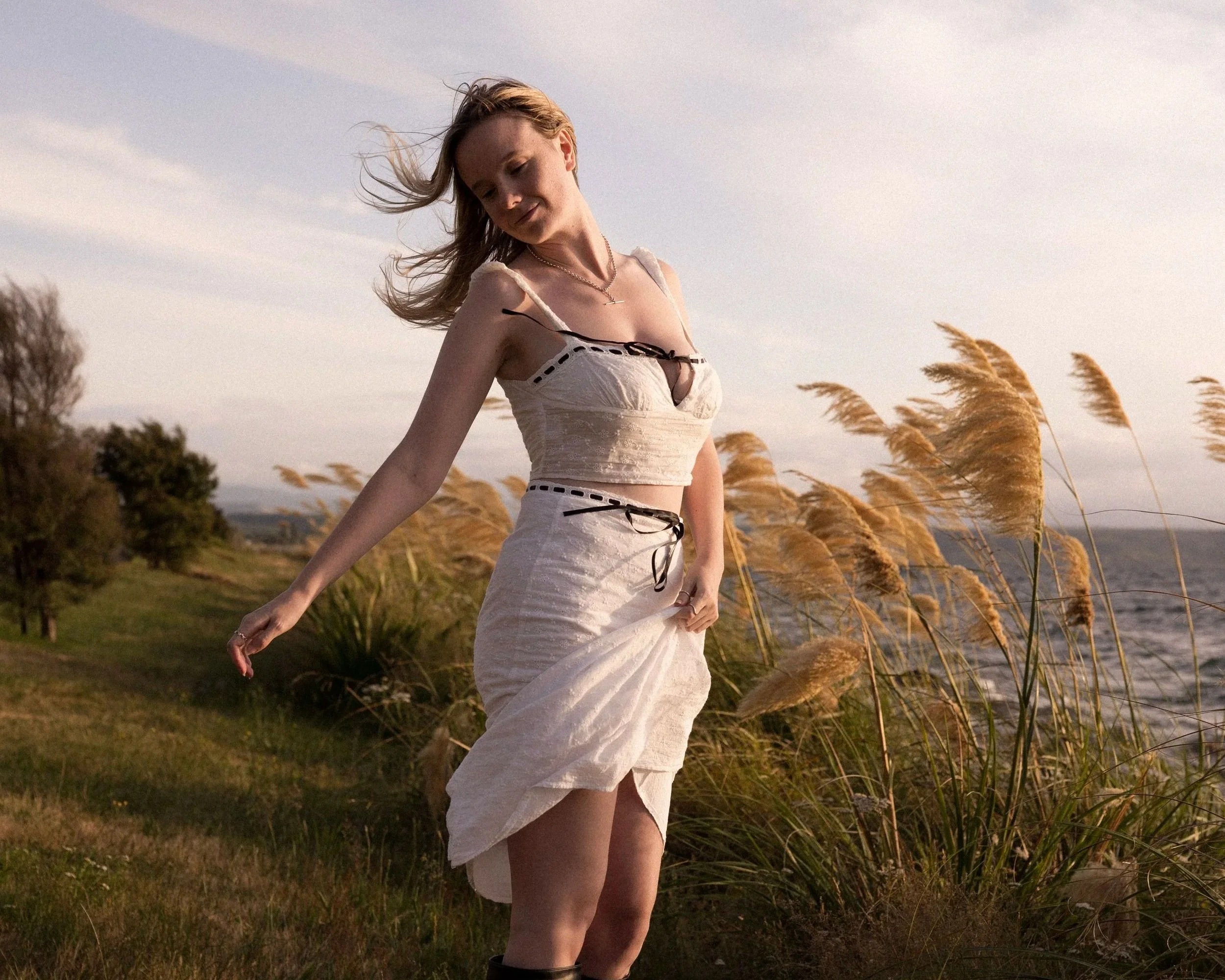 Michaela Tutty, a Somatic Sex Coach, standing in long grass by the water in Taupō, New Zealand.