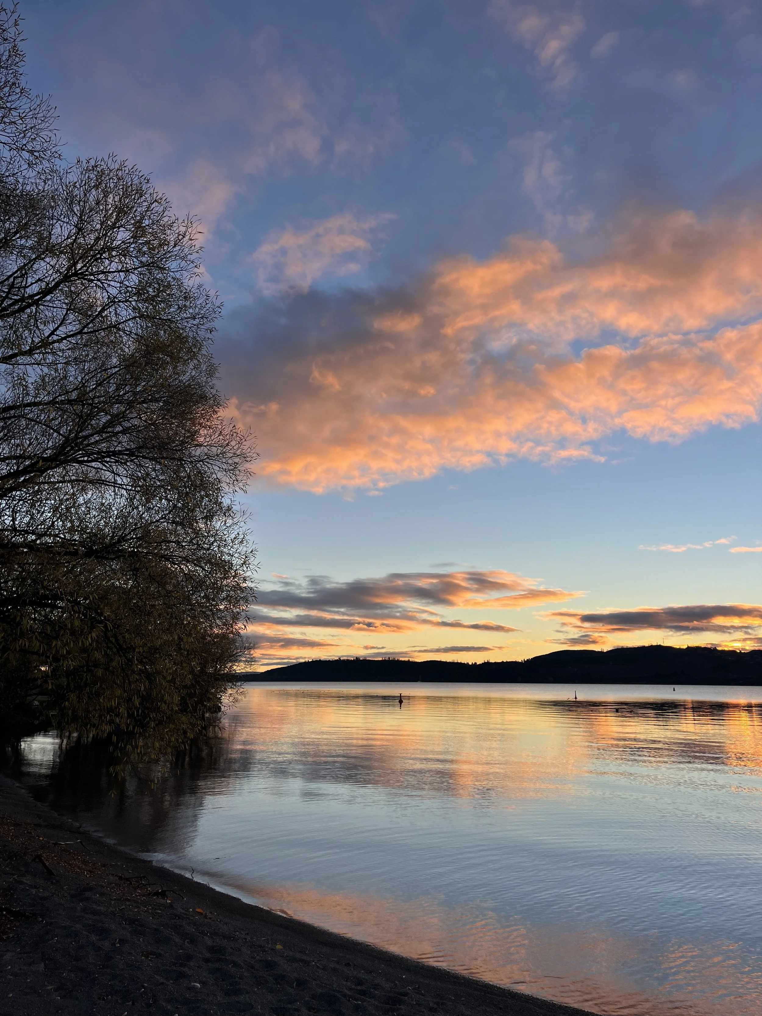 A calming scenic view of Lake Taupō in New Zealand with a blue sky reflecting on the tranquil waters, representing the serene and safe environment of Desire Pathways intimacy coaching.