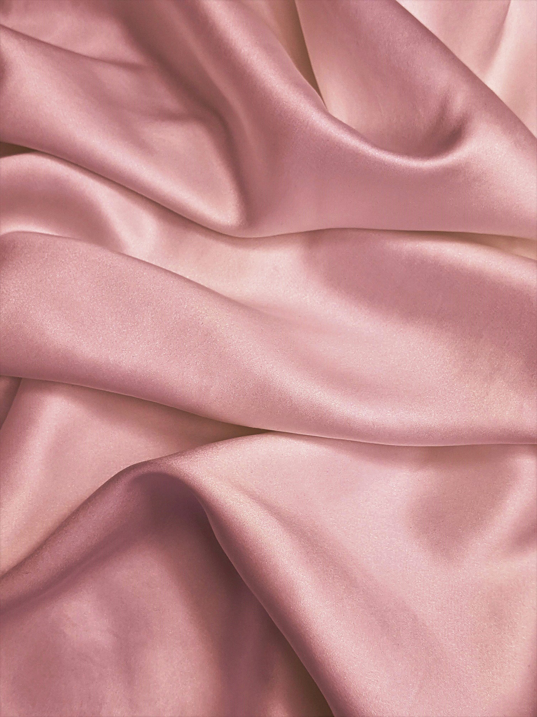 Close-up of pink satin fabric with smooth, shiny surface and folds.