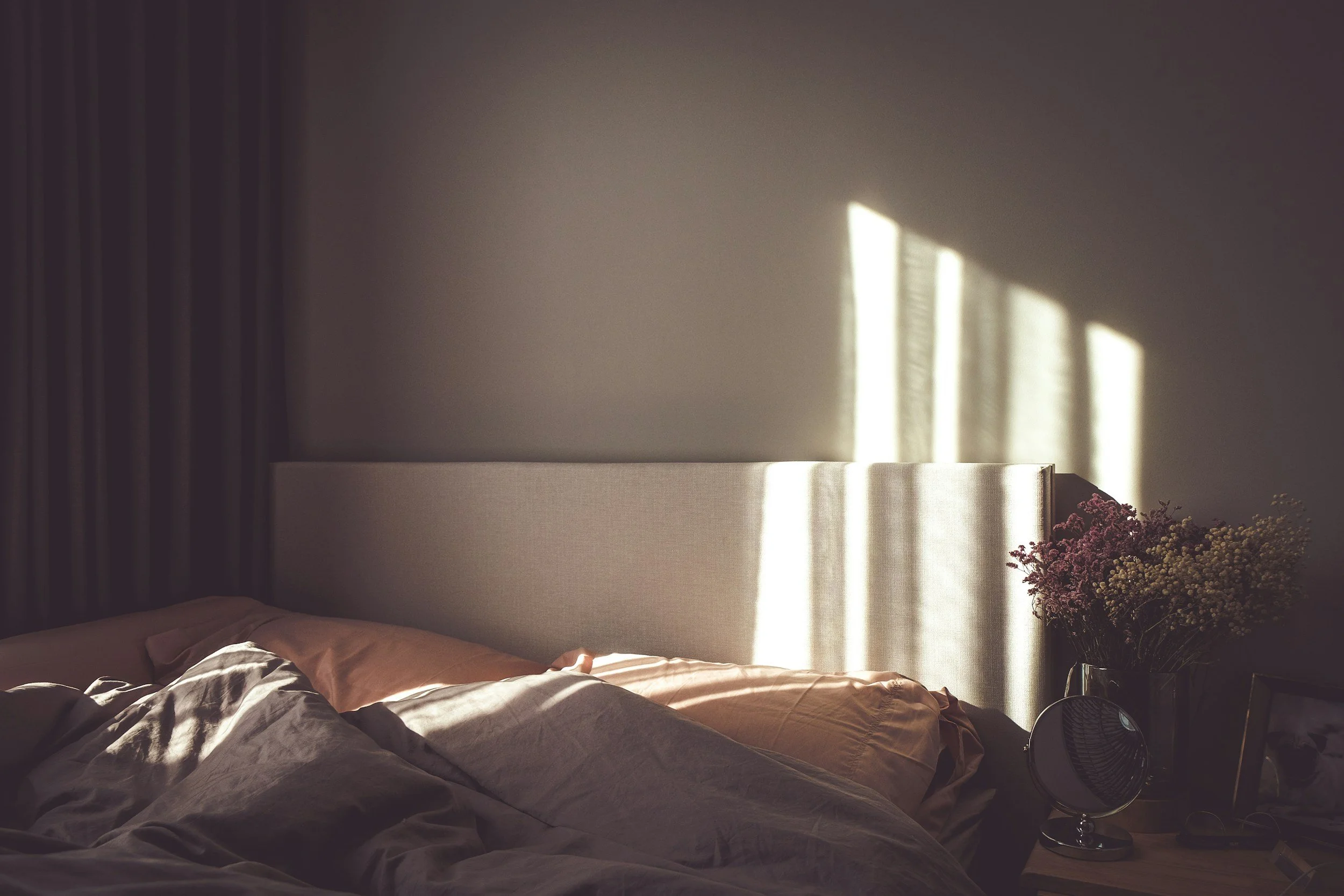 A minimalist bedroom with warm morning sunlight streaming across linen sheets and an unmade bed, creating a grounded and inviting atmosphere