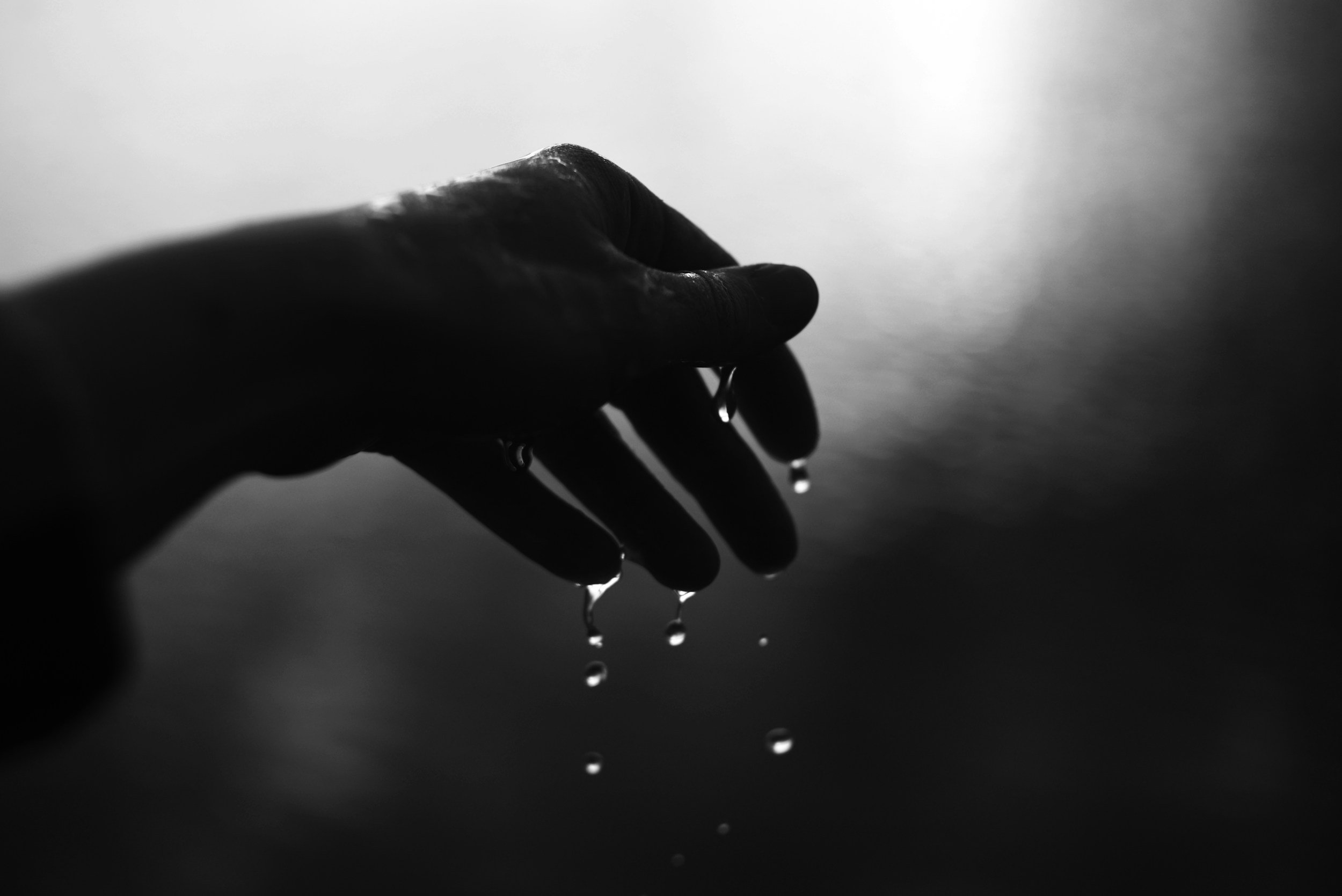moody, black-and-white artistic shot of water drops falling into an open hand, representing natural moisture and somatic awareness.